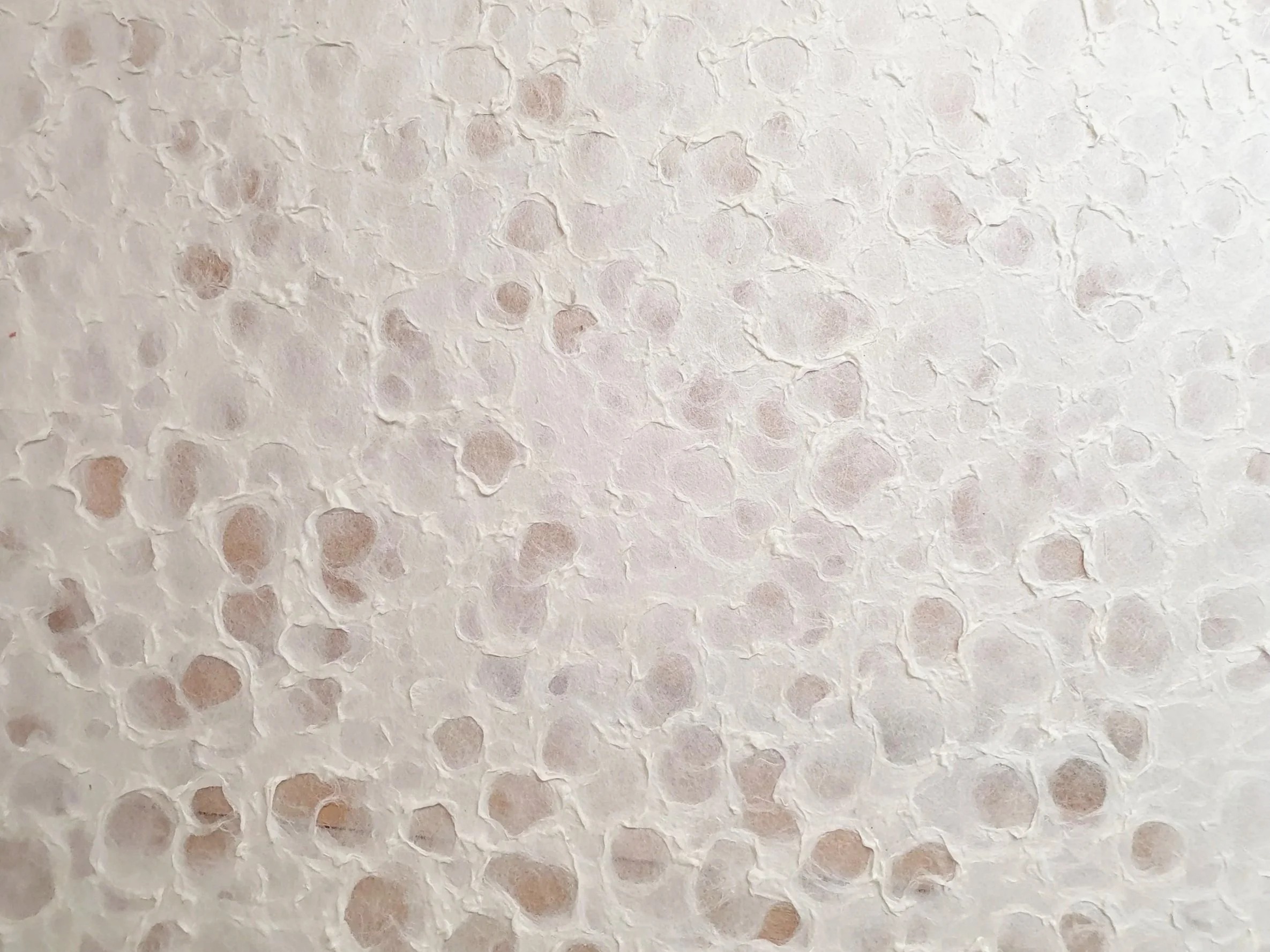 Texture de surface en papier avec des trous irréguliers, blanc avec des nuances de rose pâle.