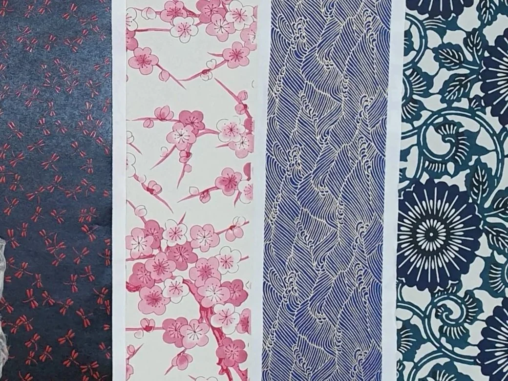 Quatre échantillons de tissus avec différents motifs : un motif de petits dragonflies rouges sur fond bleu, des branches de cerisiers en fleurs roses sur fond blanc, un motif géométrique bleu et blanc avec des lignes ondulées, et un motif floral bleu foncé avec des fleurs et des feuilles stylisées.