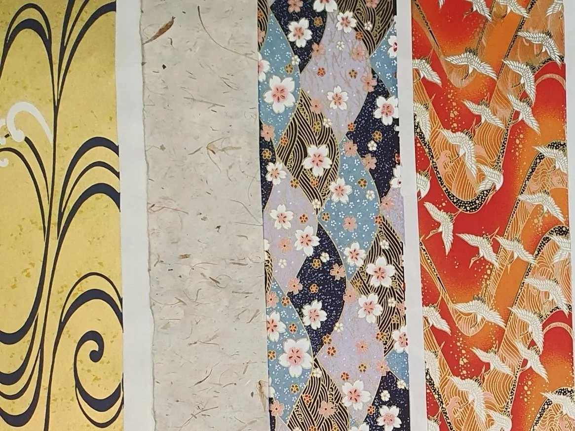 Quatre bandes de papier japonaises avec des motifs traditionnels, comprenant des dessins de vagues, de fleurs de cerisier, et des grues, dans des couleurs jaune, beige, bleu floral et rouge orangé.