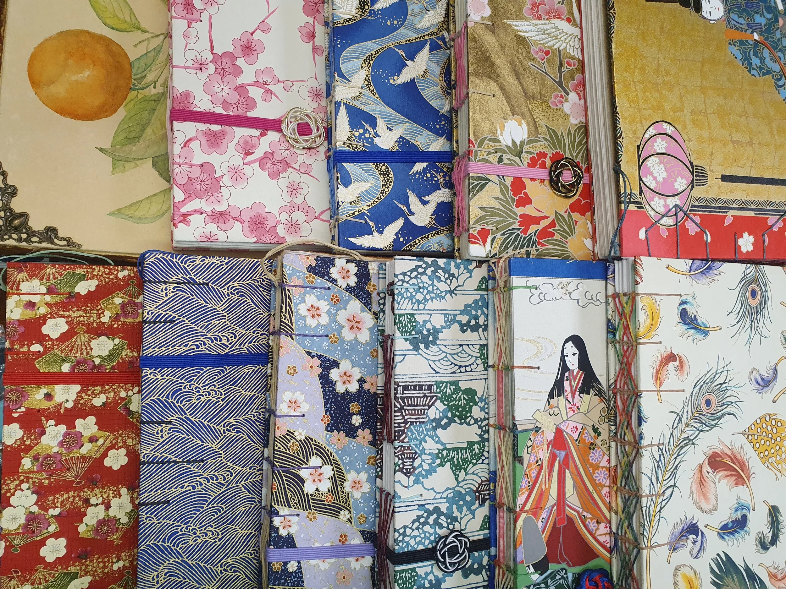 Collection de boîtes en papier décoratives aux motifs japonais traditionnels, représentant des fleurs, des paysages et des figures féminines en kimono.