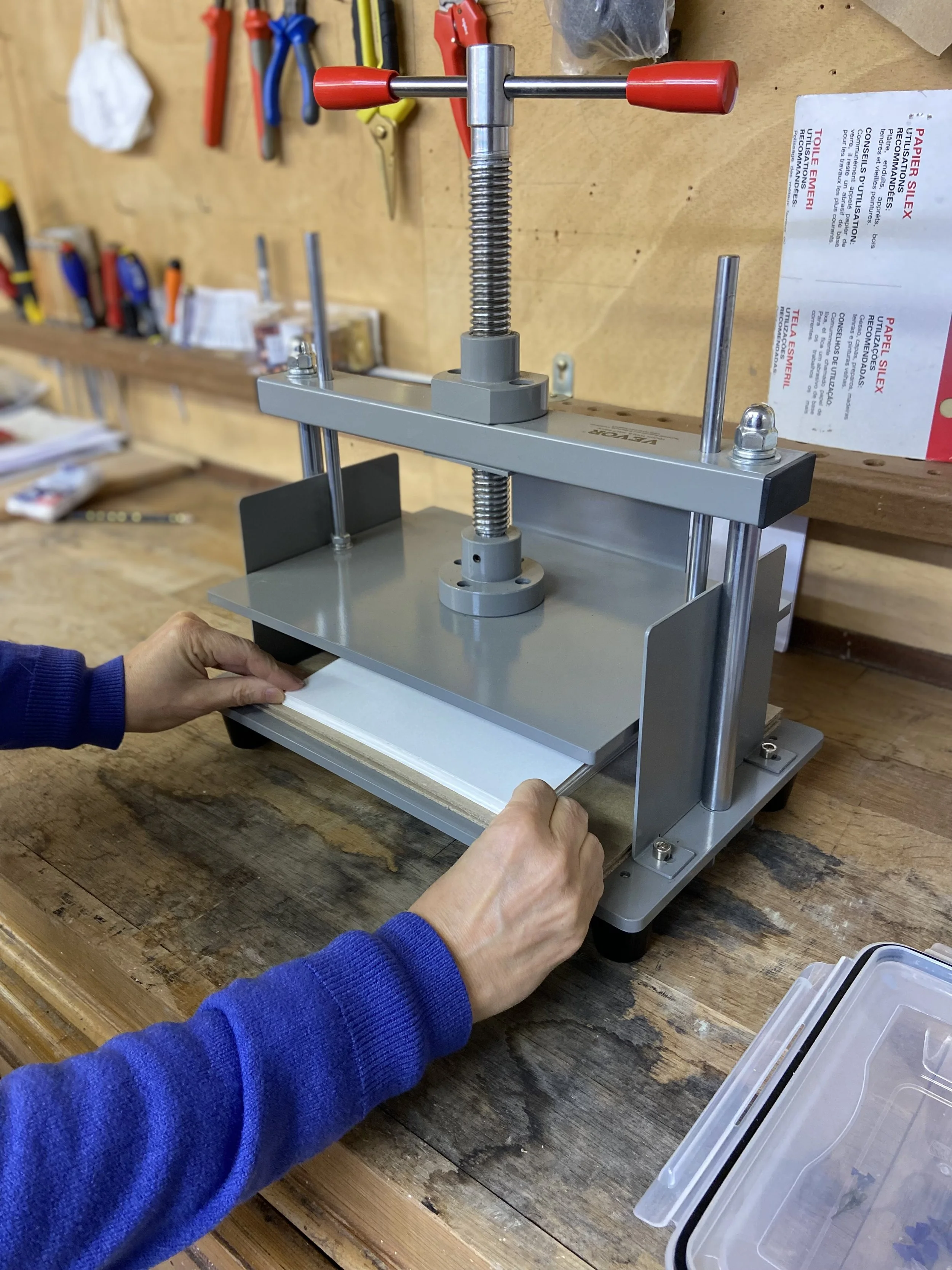 Une machine à appuyer ou presser des plaques ou feuilles en métal ou plastique, avec une main d'une personne ajustant une feuille sur la plaquette, dans un atelier de bricolage.