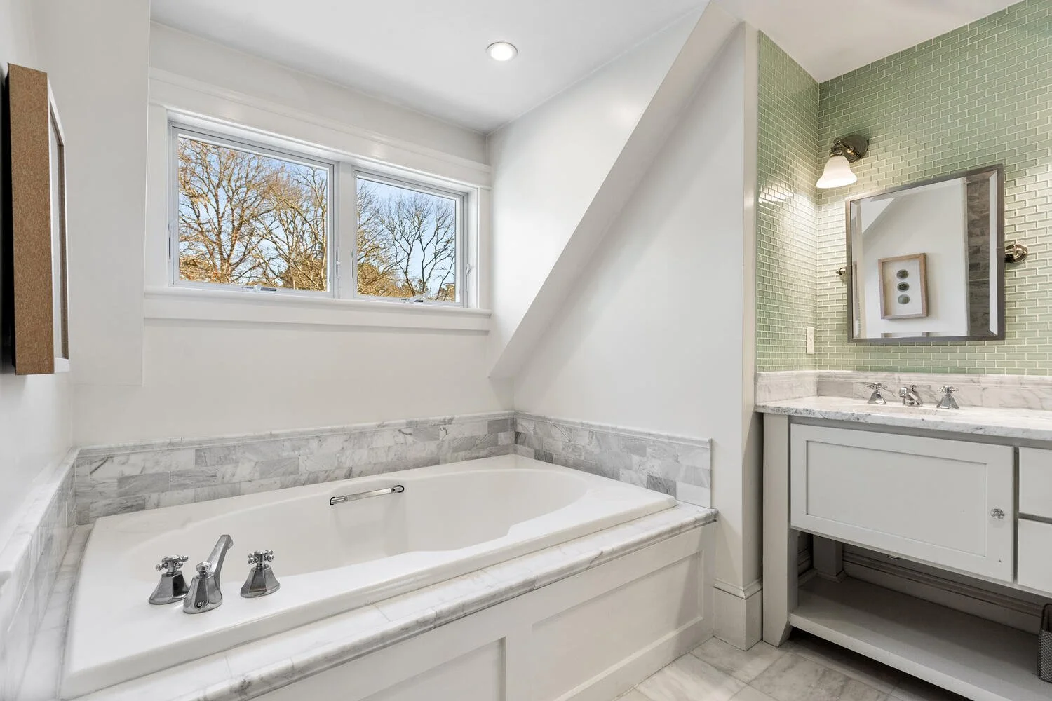Bathroom with a bathtub near a window and a vanity with a mirror and green tiled wall.