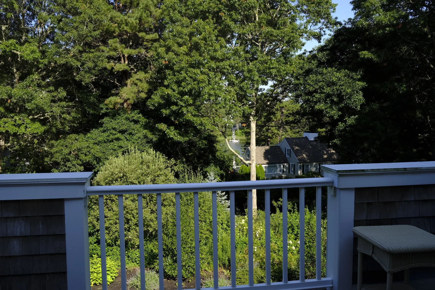 View from a porch showing green trees, shrubs, houses, and a blue sky.