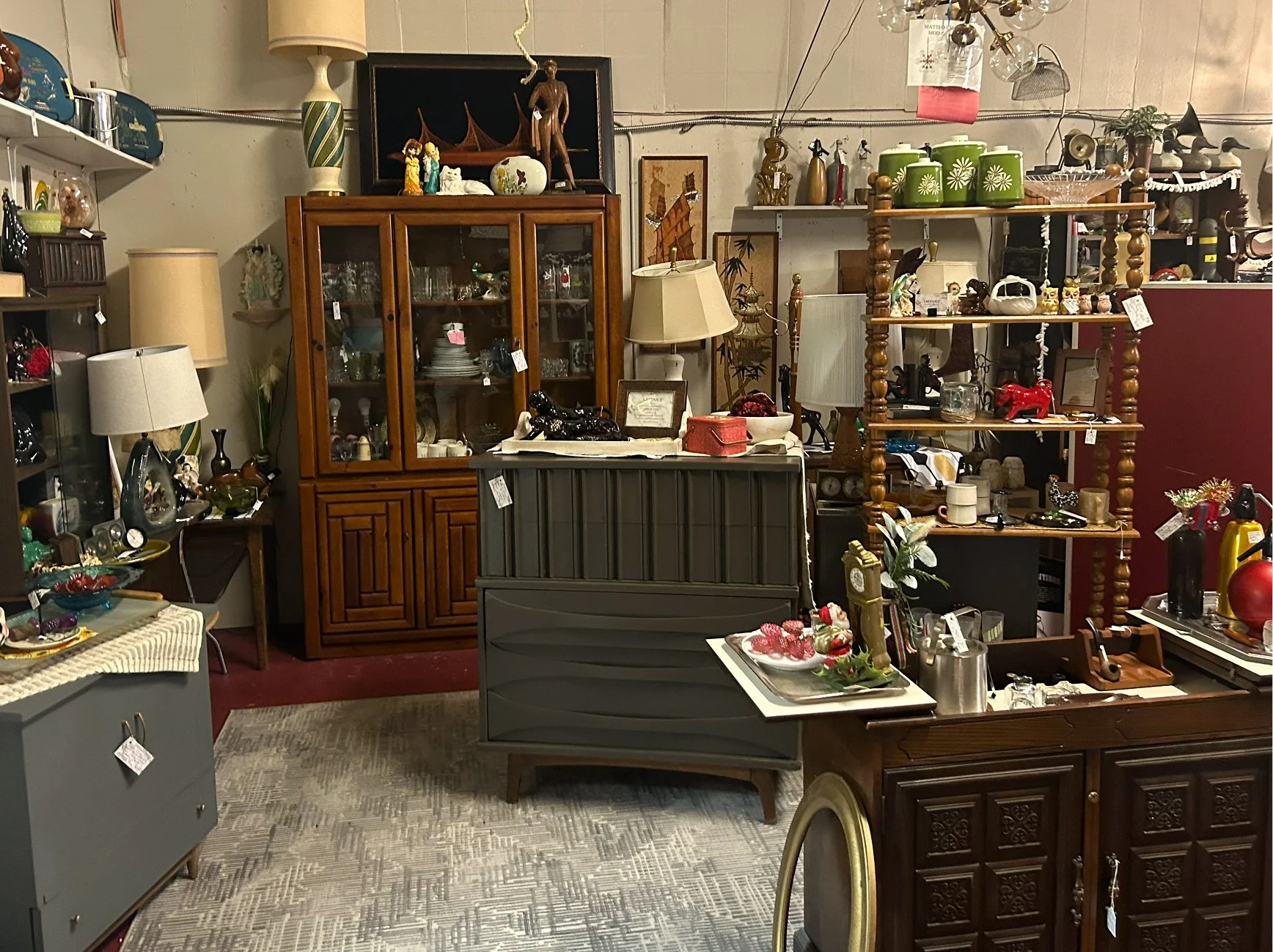 A room filled with vintage furniture and various knickknacks, including glassware, lamps, decorative figurines, and ceramics, arranged on shelves, tables, and cabinets.