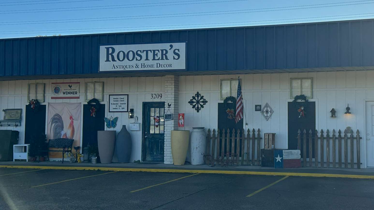 Exterior of Rooster's Antiques & Home Decor storefront with patriotic decorations and vintage decor items outside.