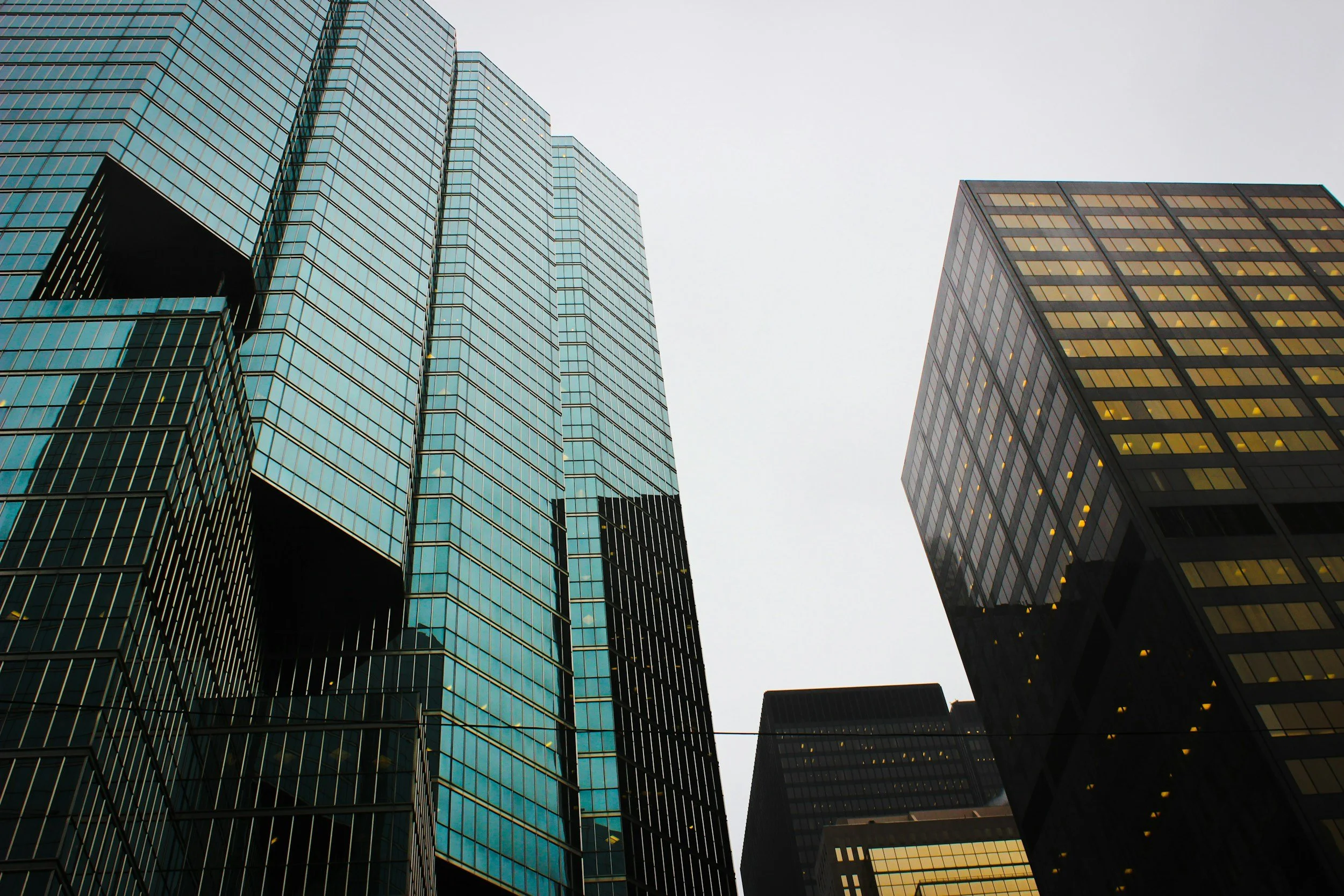 Tall skyscrapers with glass facades in a cityscape, under an overcast sky.
