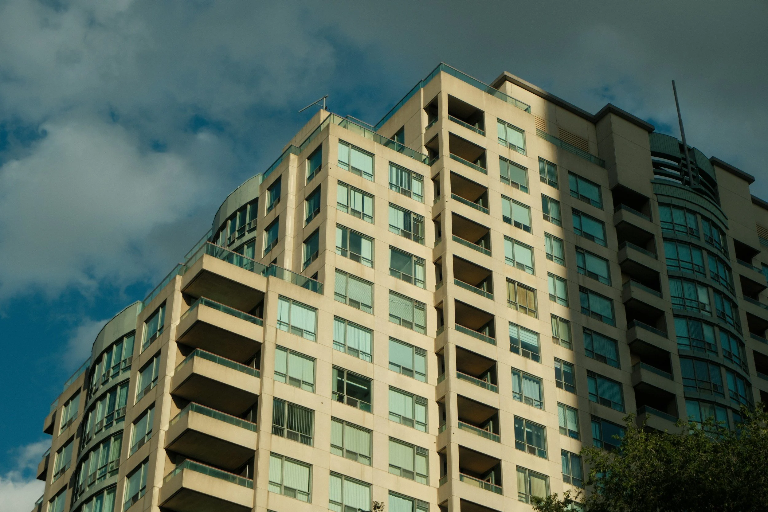 High-rise apartment building with numerous windows and balconies against a blue sky with clouds.