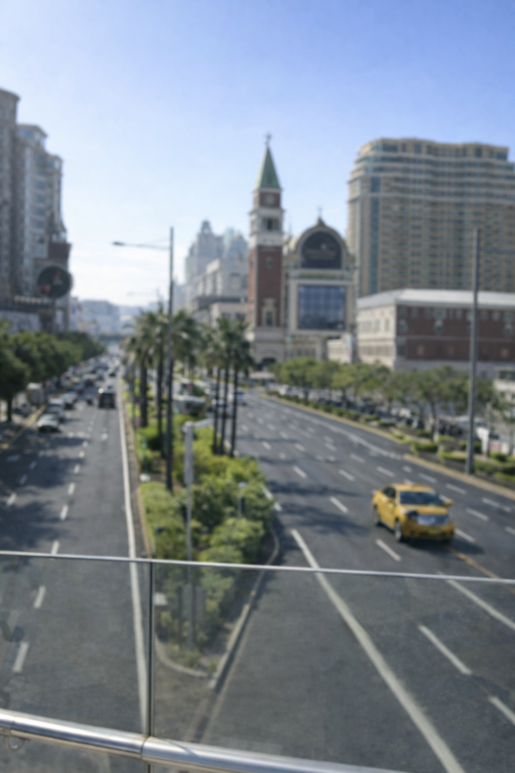 Blurred city street view with cars, palm trees, and tall buildings under a clear blue sky.