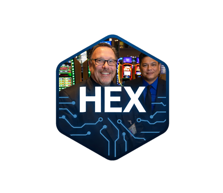 Two men in suits standing in front of slot machines, with a digital overlay featuring the word HEX and circuit patterns.