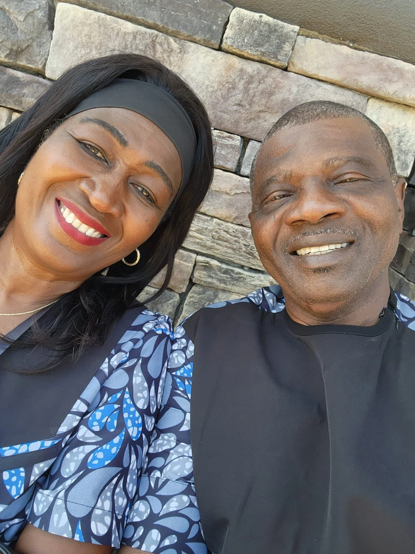 A woman and a man smiling for a selfie in front of a stone wall.