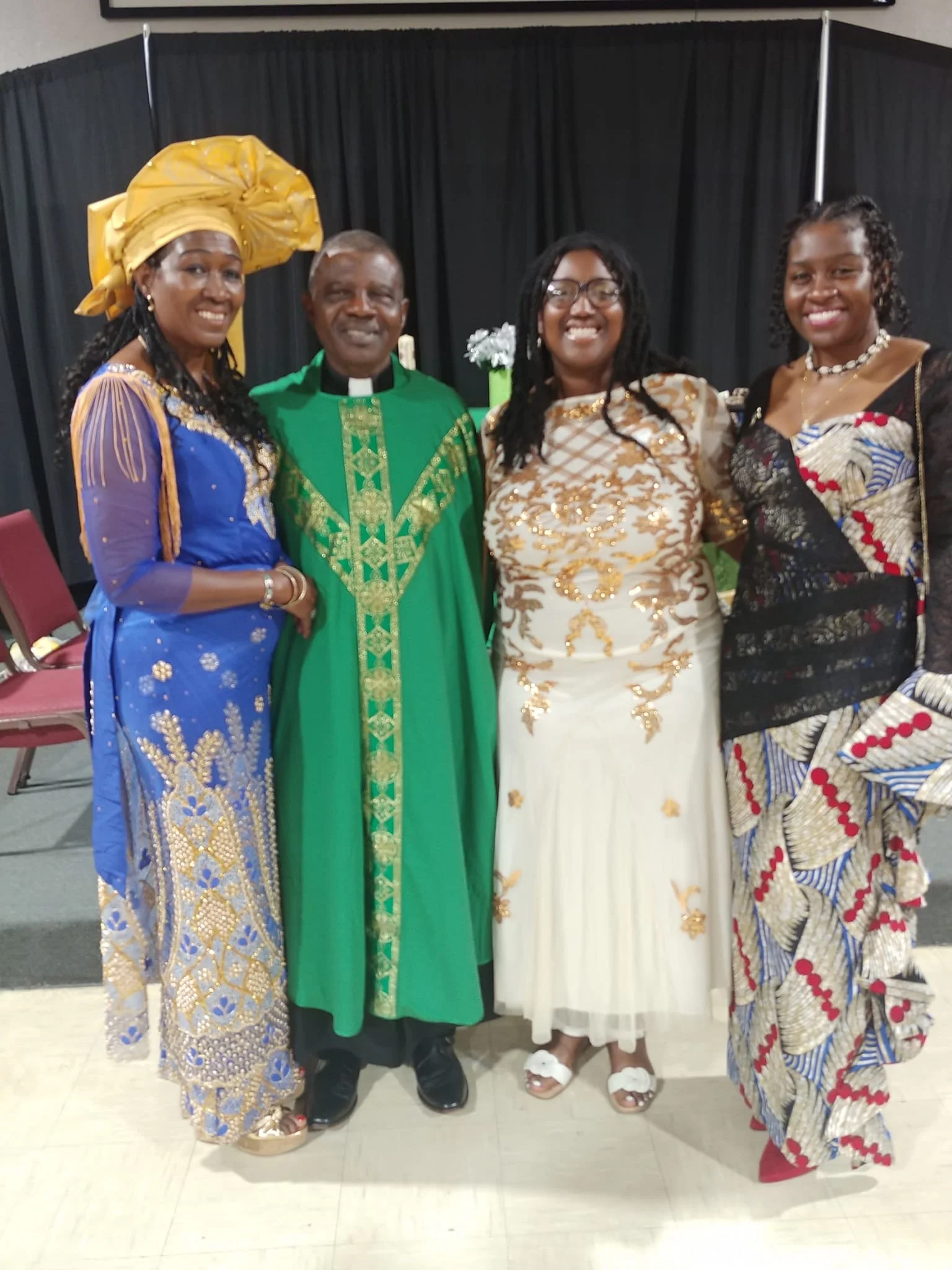 Four people in colorful traditional African attire standing together indoors, smiling at the camera.