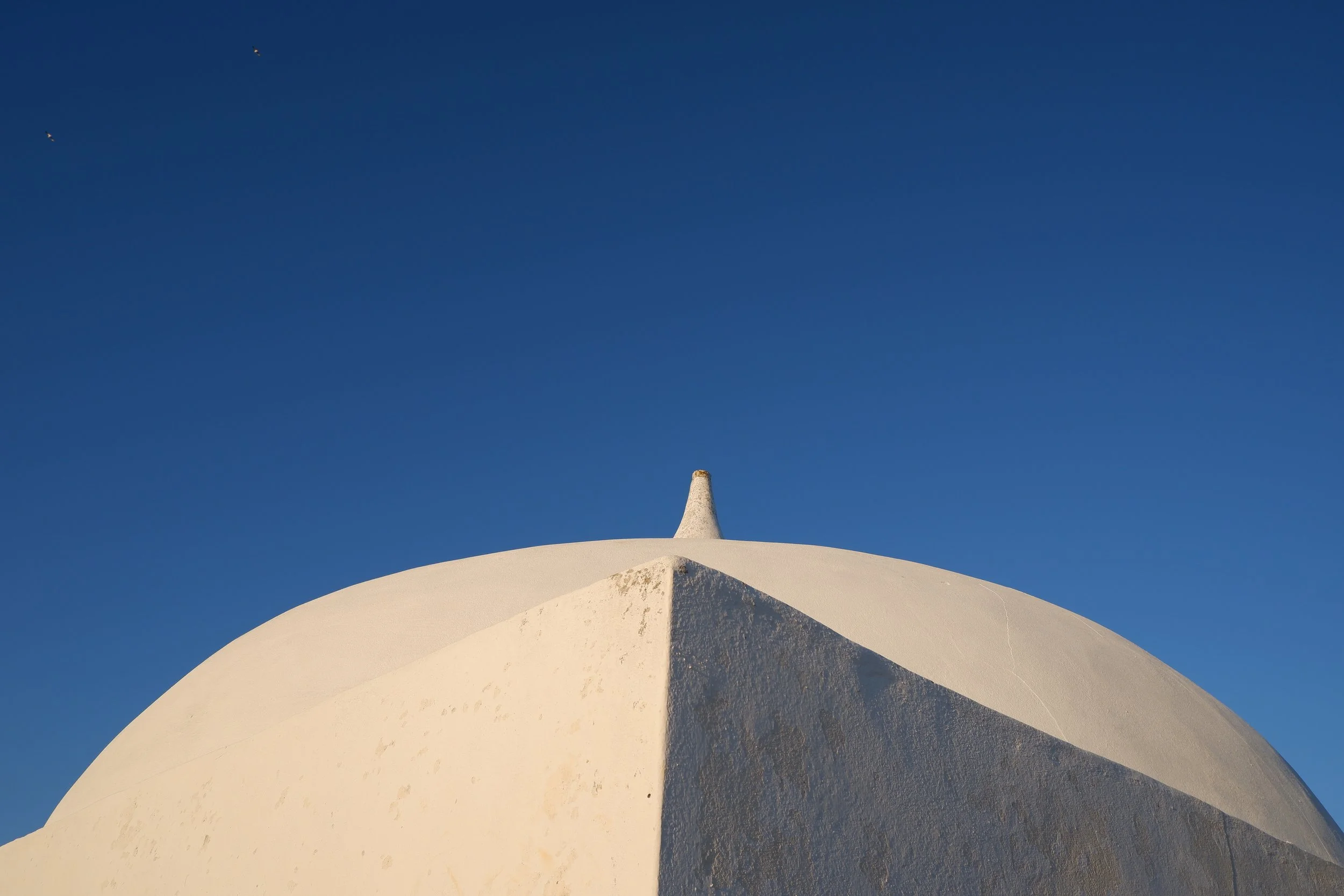 A white, rounded architectural structure with a pointed top against a clear blue sky.