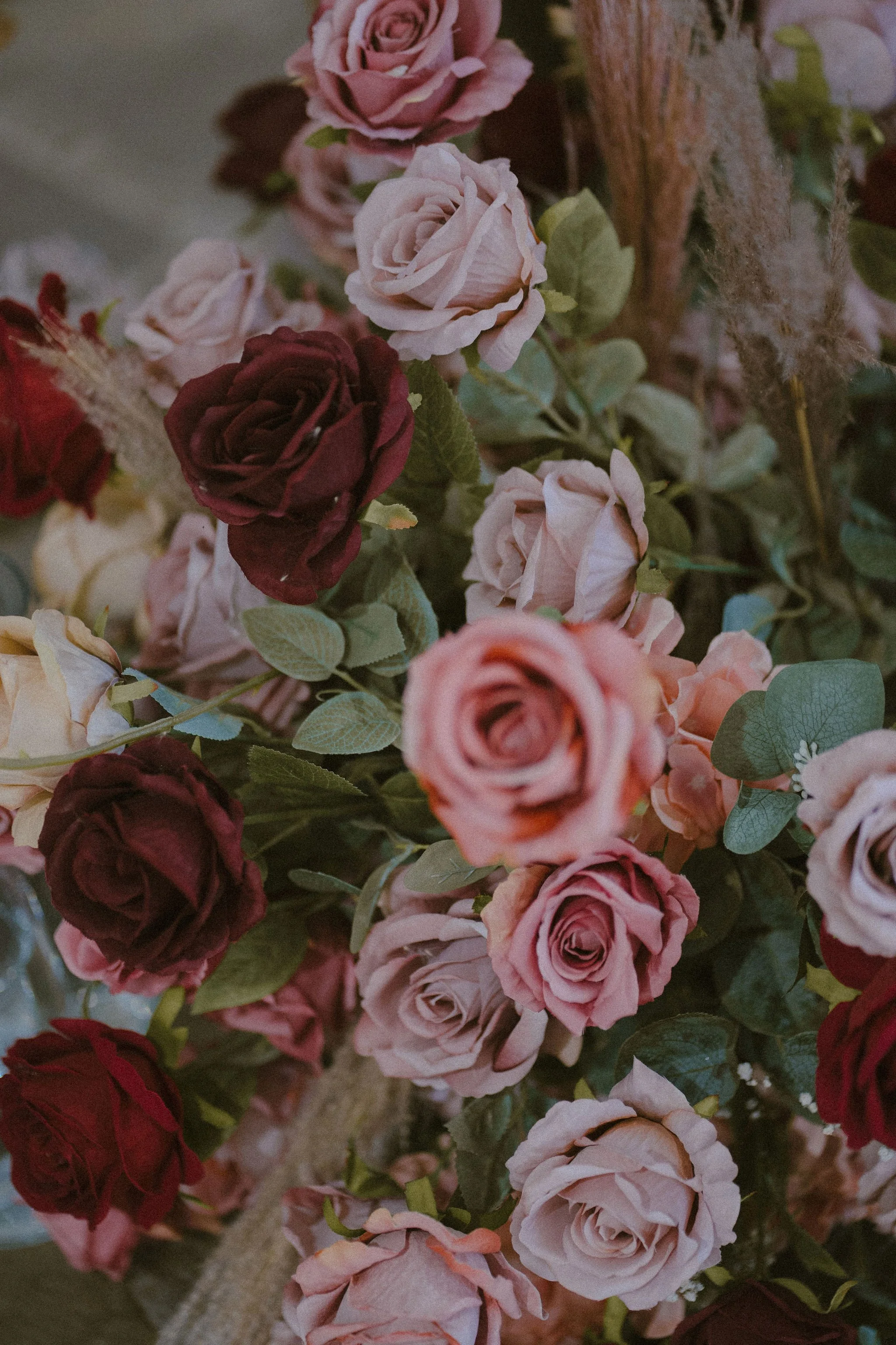 A close-up of a bouquet of artificial roses in shades of pink, red, and cream, with green leaves and decorative elements in the background.