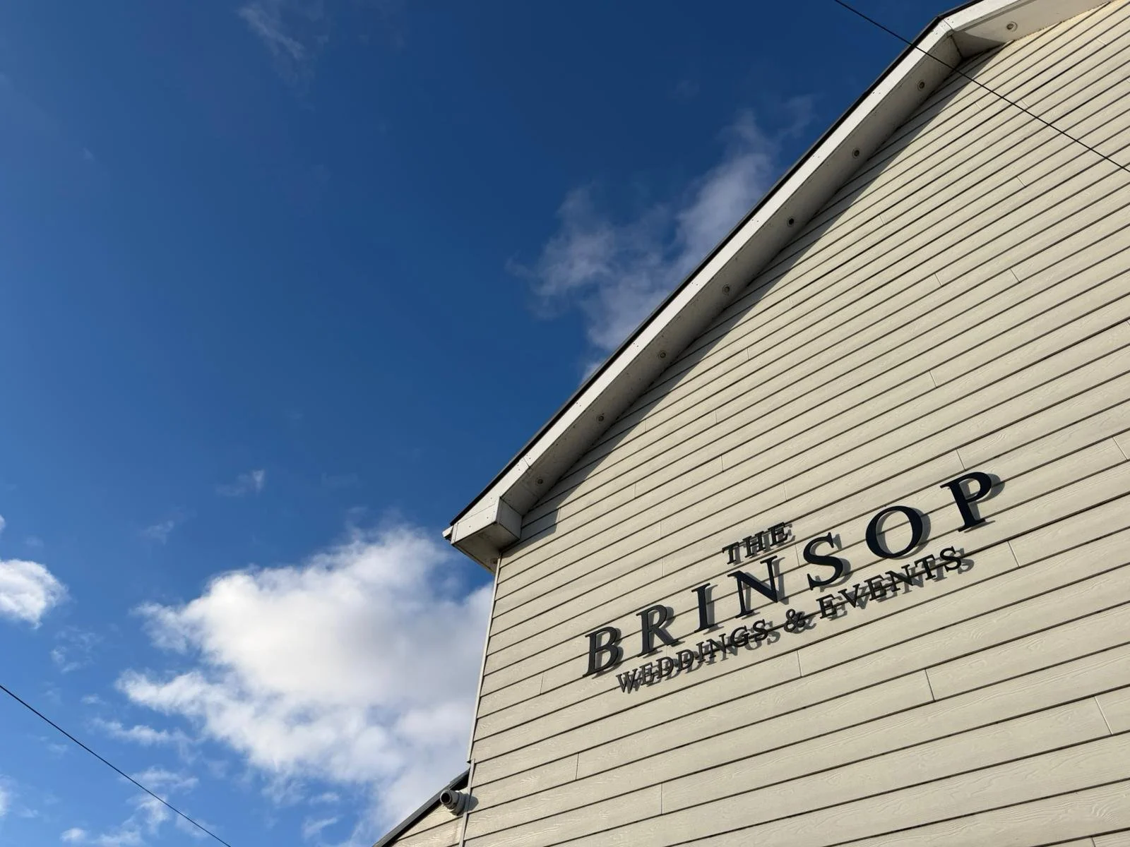 The side of a building with a sign that reads 'The Brinsop Weddings & Events' against a blue sky with some clouds.