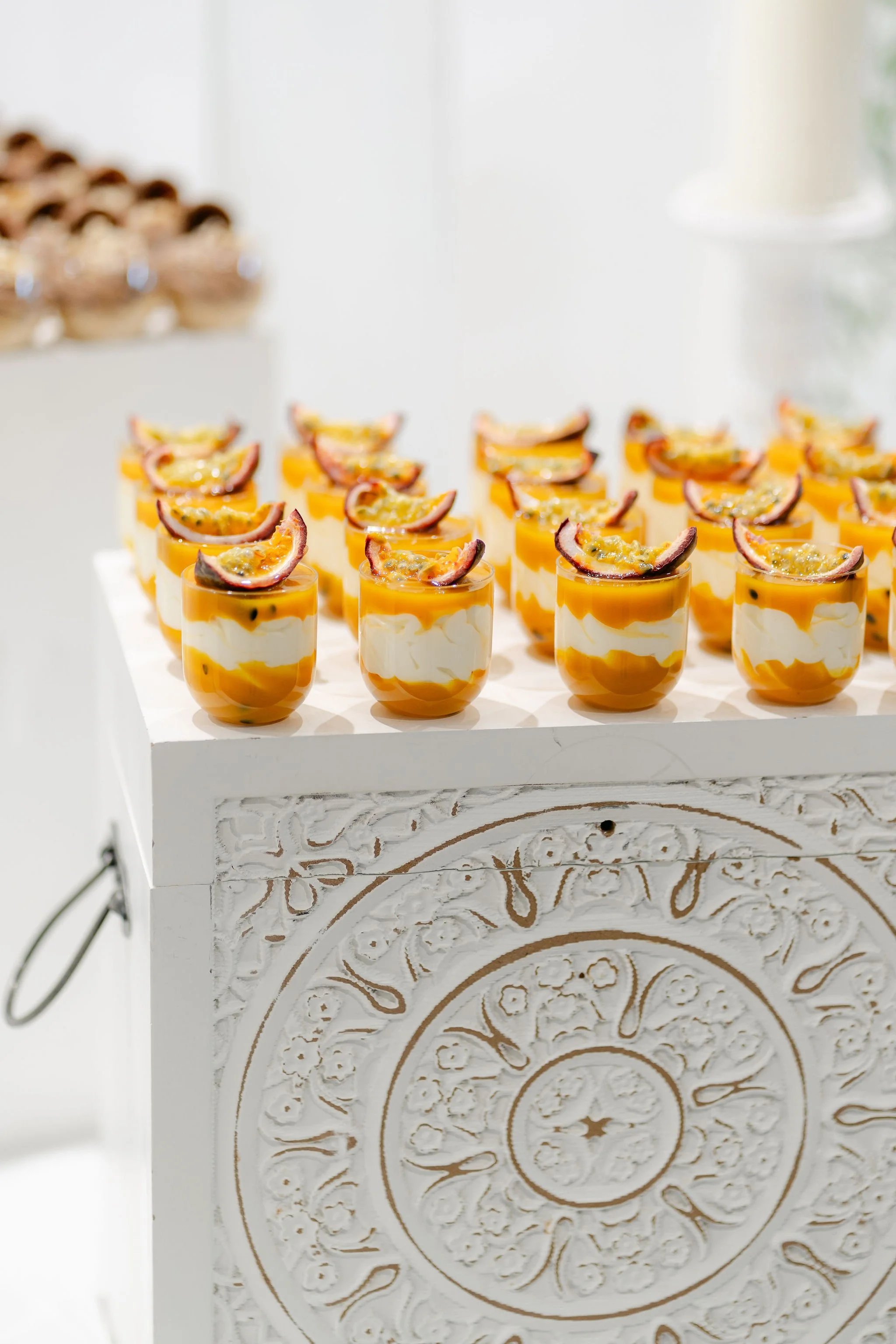 Row of passion fruit and yogurt desserts topped with passion fruit slices on a white decorative table.