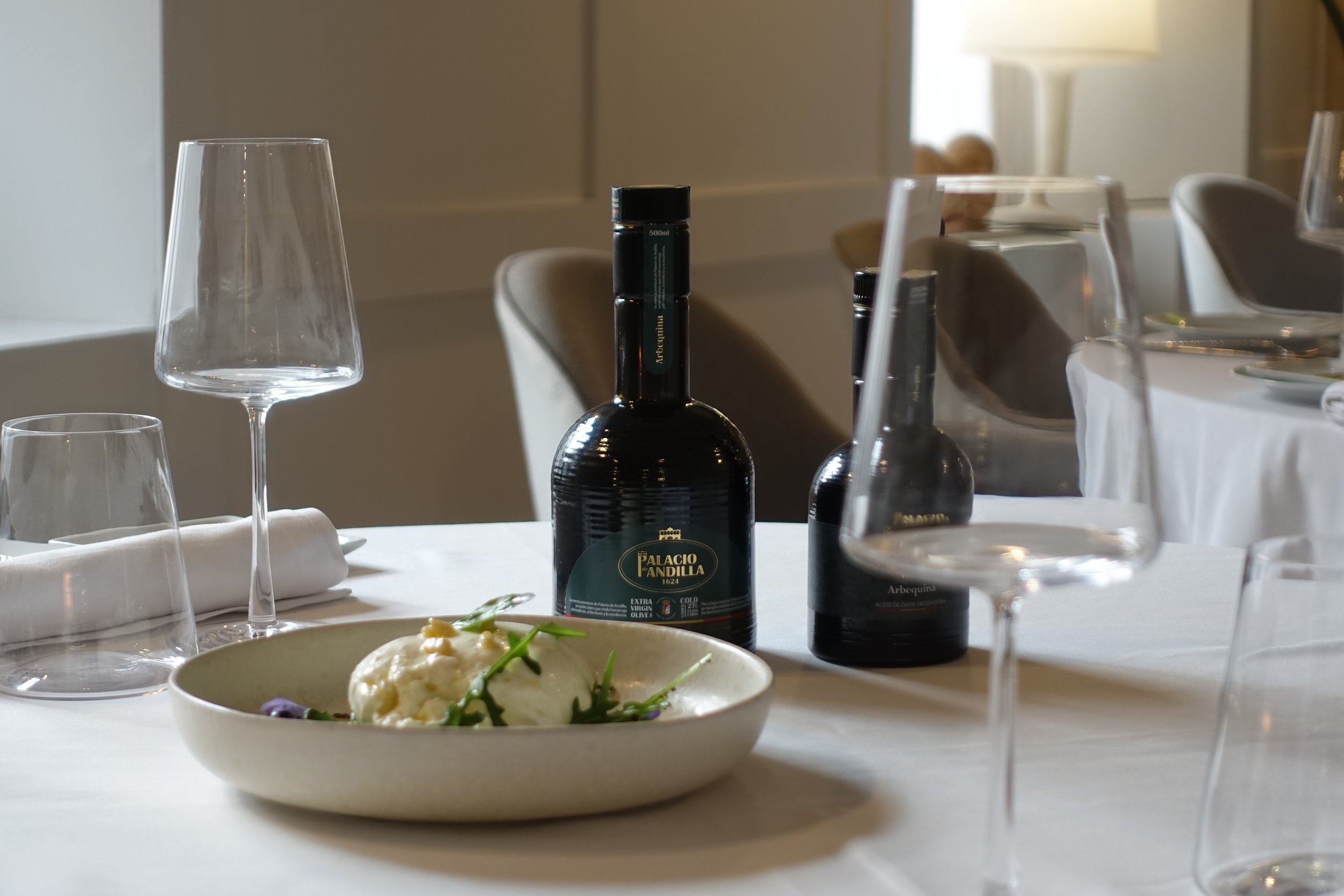 Mesa en restaurante con plato de comida, botella de vino, copas de vino y agua, y cubiertos.