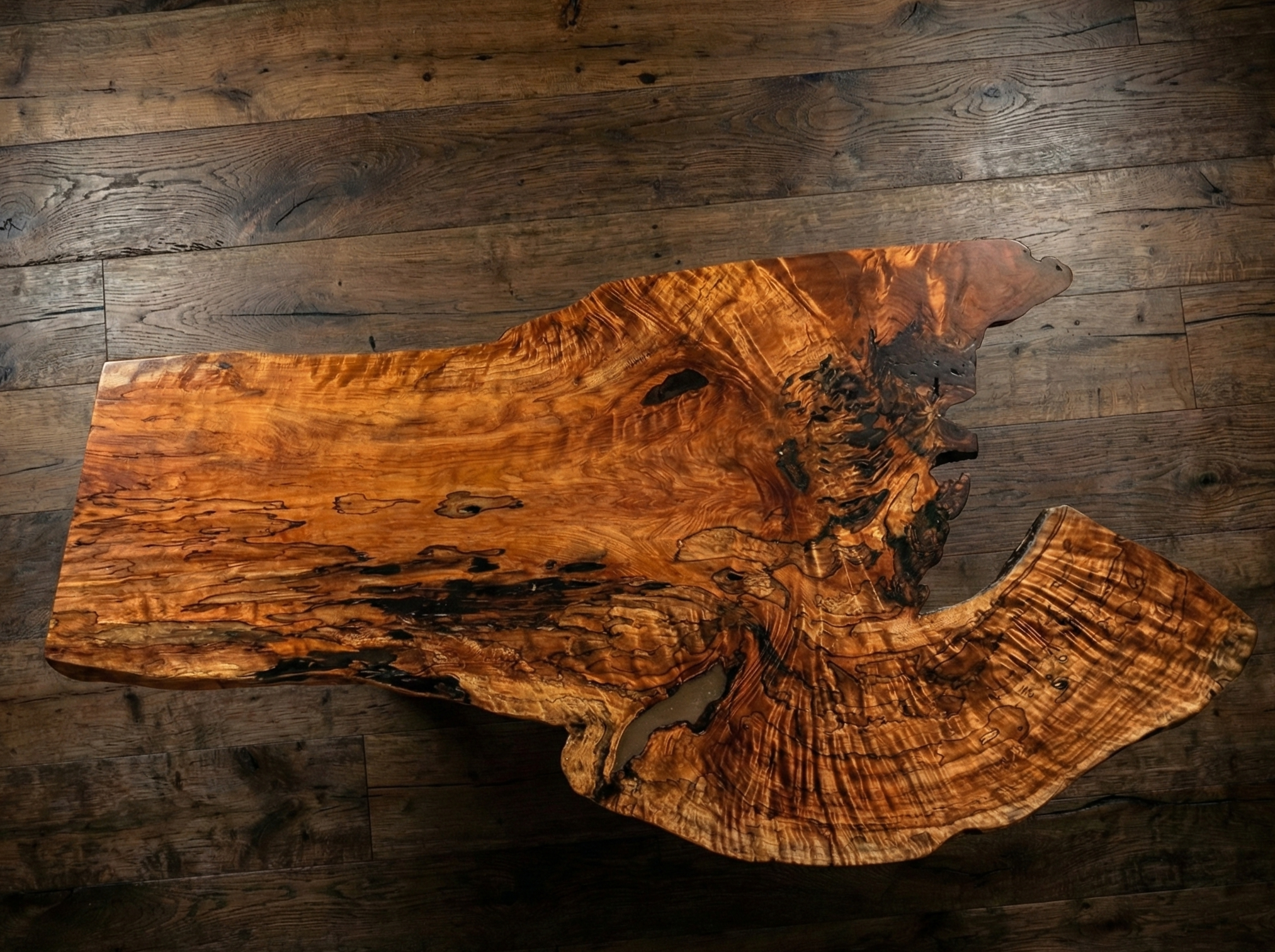 A large, irregularly shaped wooden table with a natural edge, made from a single slab of wood, placed on a wooden floor.