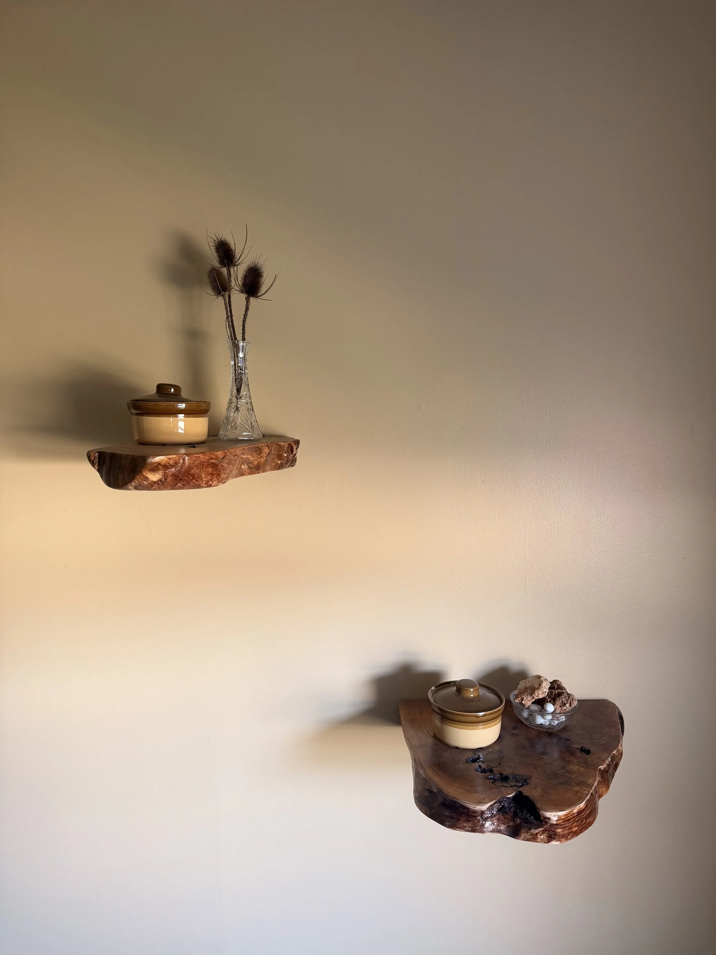 Two wooden wall shelves with ceramic containers and decorative items, one shelf is mounted on the wall and the other is below it, with a beige wall background.