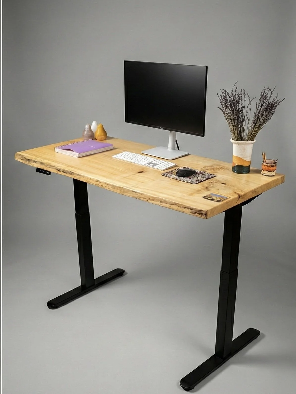 Standing desk with a monitor, keyboard, mouse, purple notebook, small decorative vases, and a large vase with dried lavender.