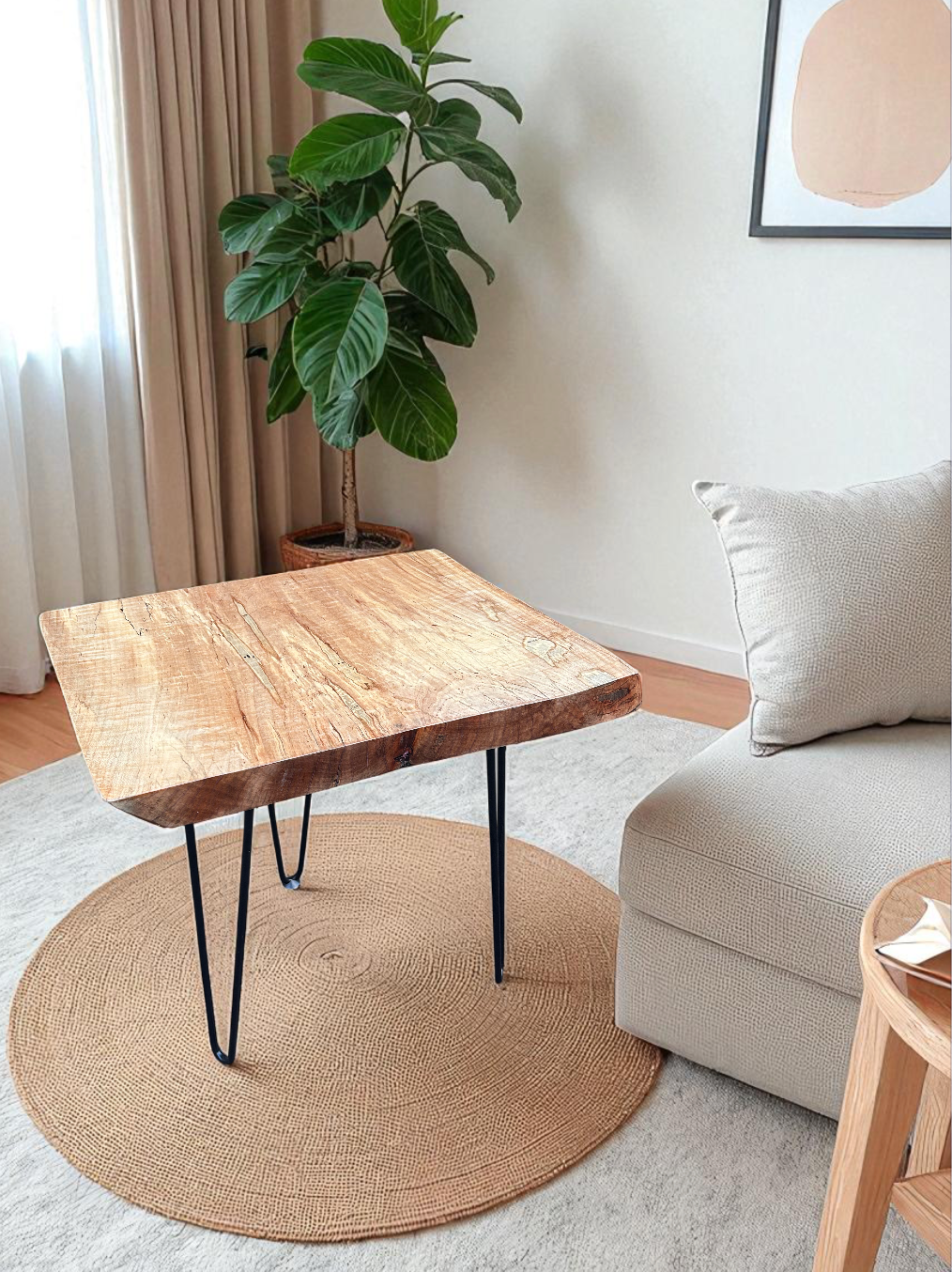 A living room corner with a wooden side table on a circular woven rug, a large green potted plant with broad leaves, a beige sofa with a pillow, and a framed abstract art piece on the wall.