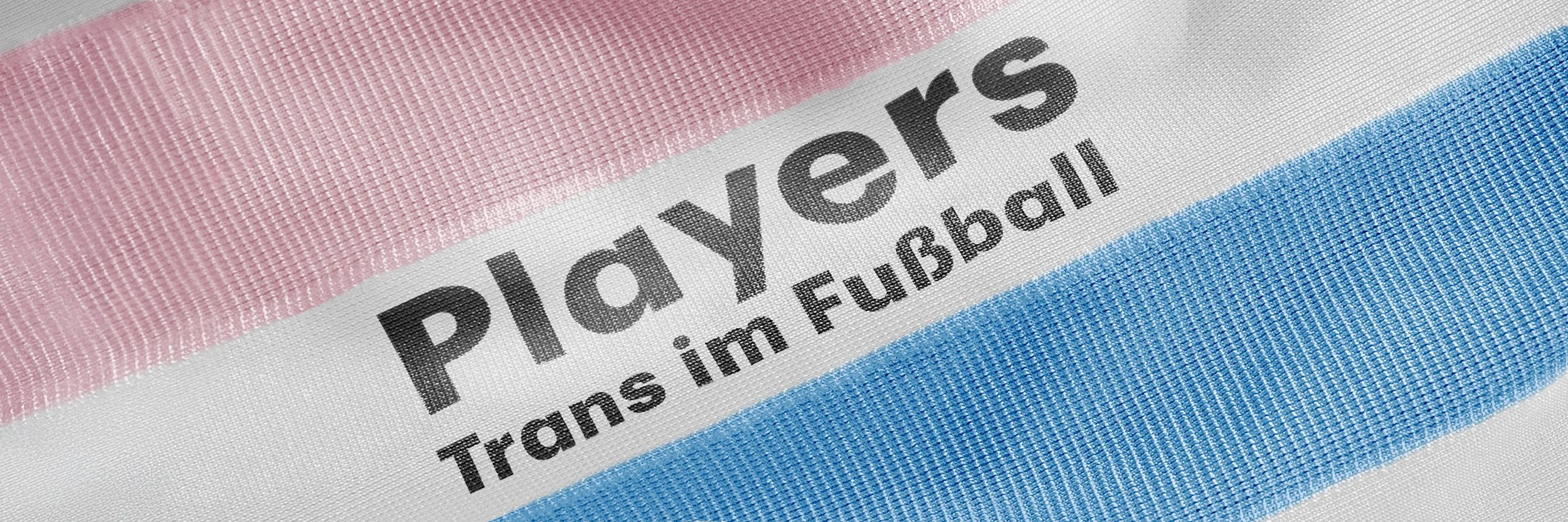 Close-up of a fabric label on a PlayStation 5 box with pink, white, and blue stripes and the text 'PlayStation', 'Trans im EuroBall' in black.