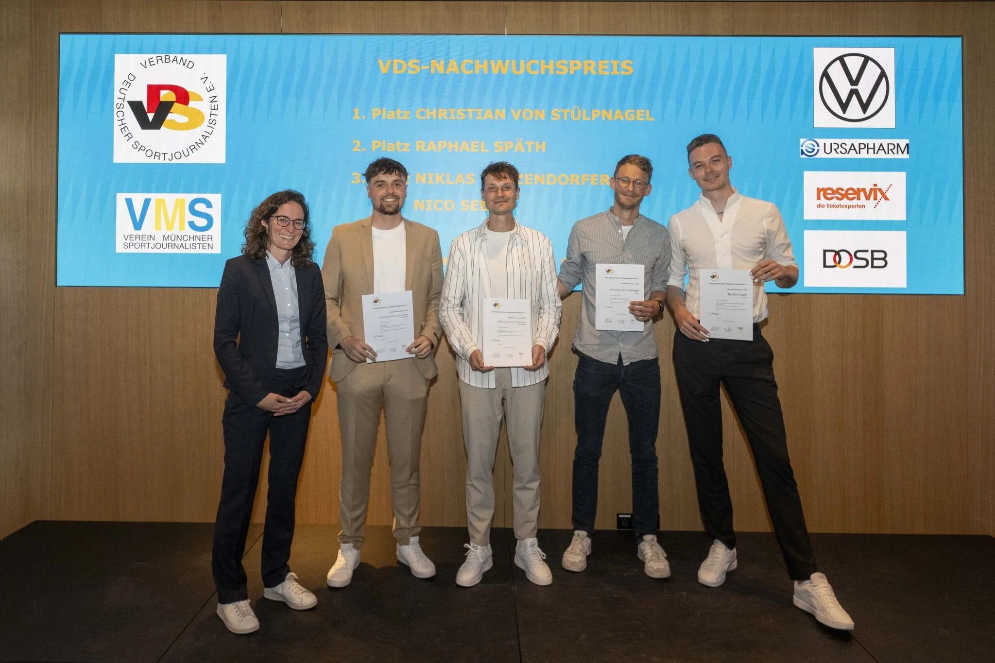 Five young adults standing on a stage in front of a large screen, holding certificates, smiling for a photo. The screen displays the title "VDS-Nachwuchspreis," and logos of VW, URSAPHARM, reservix, and DOSB.
