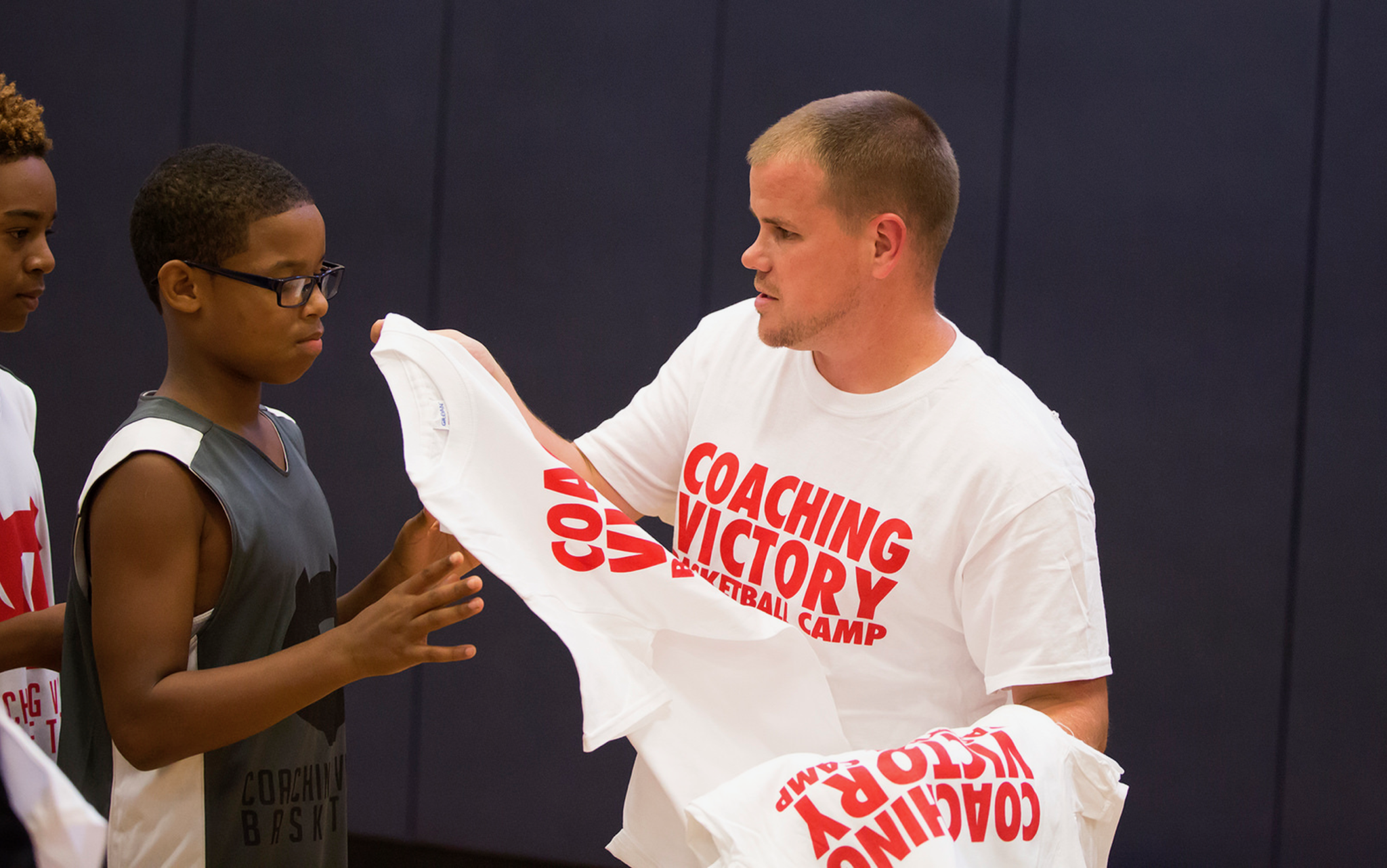 A coach handing out t-shirts to young basketball players during a coaching clinic.