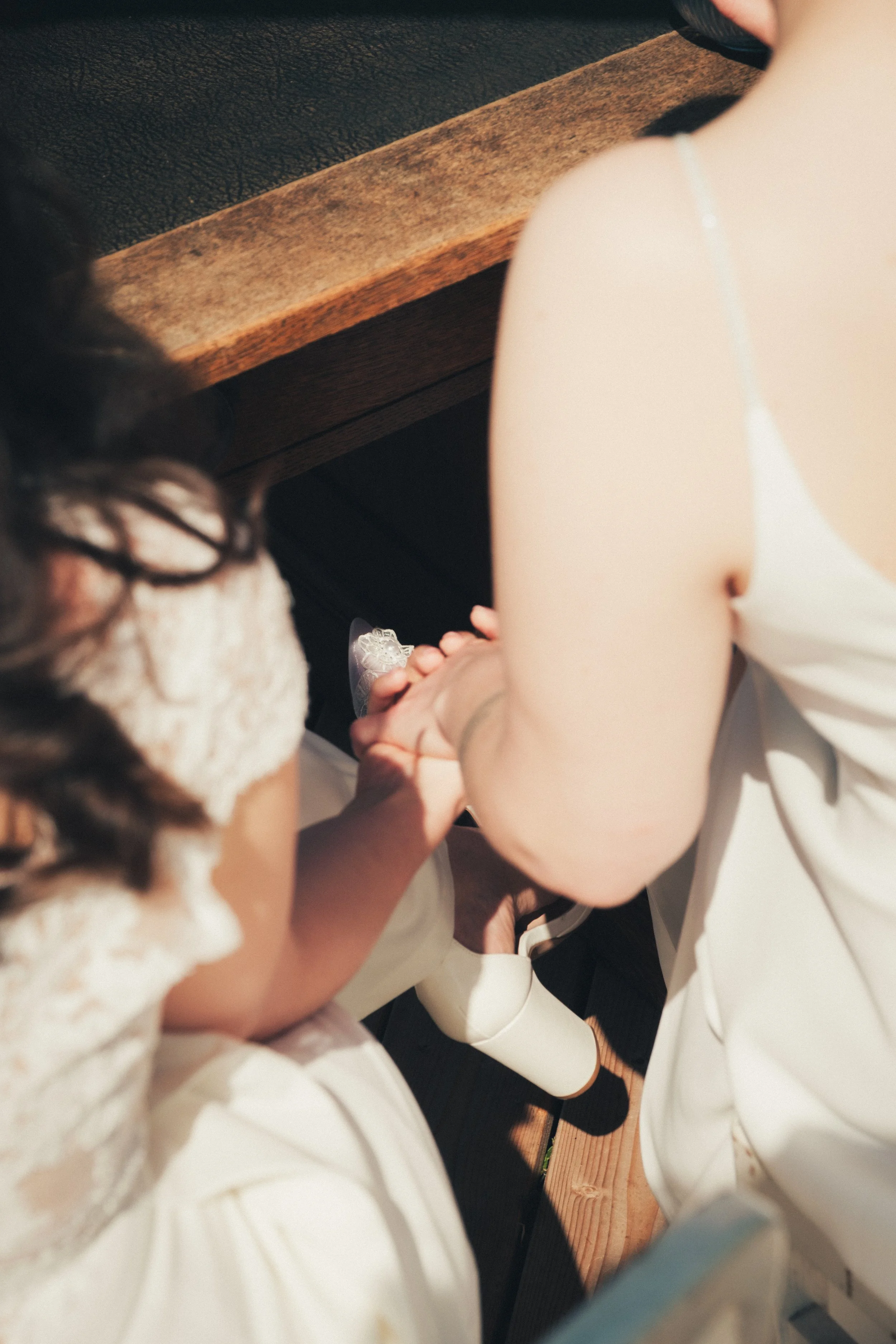 Close-up of two people holding hands, one wearing a white dress, at a wooden table in a casual setting.