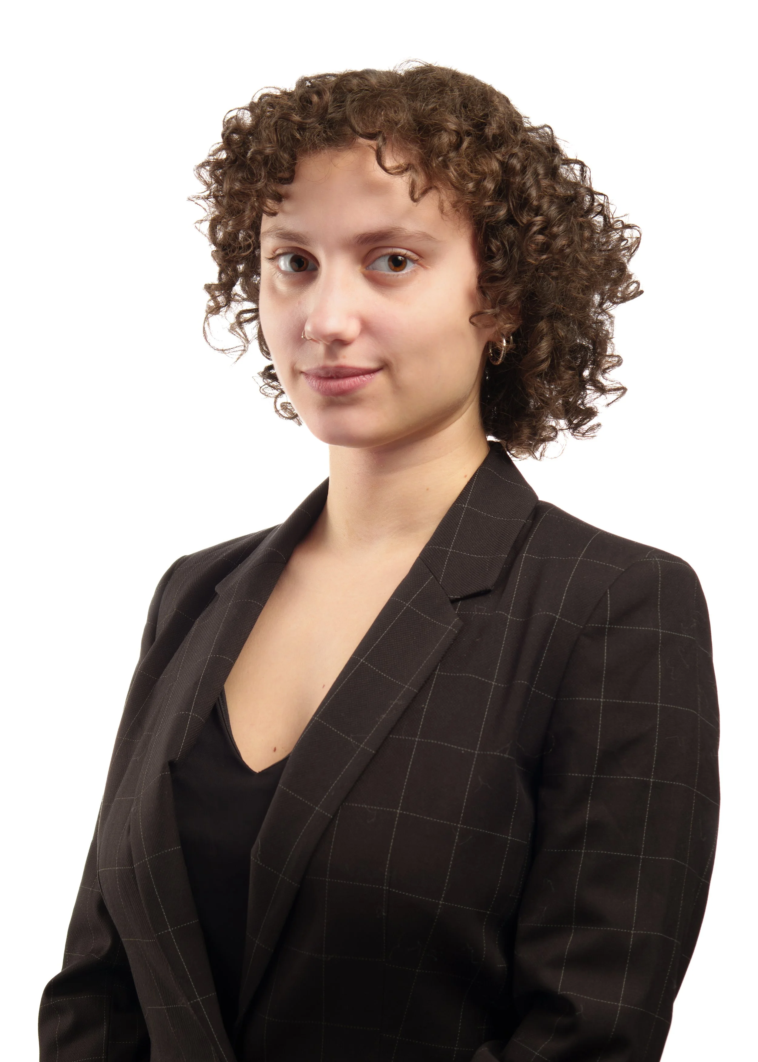 A woman with curly brown hair, wearing a black blazer with a subtle checkered pattern, standing against a white background.