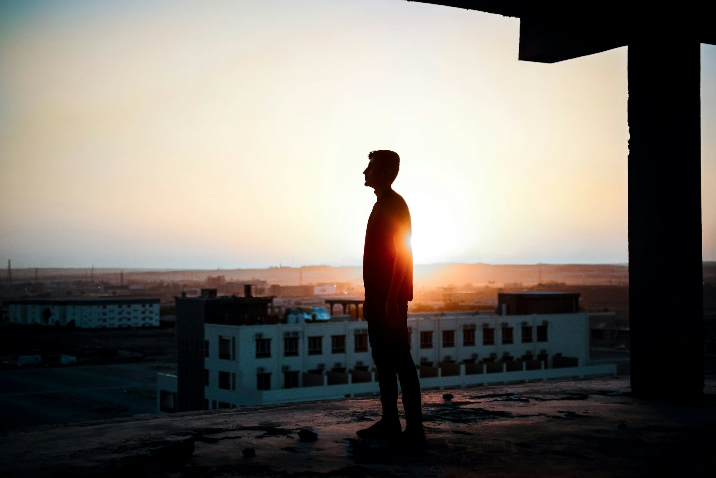 Silhouette of a man standing on a rooftop during sunset with buildings in the background.