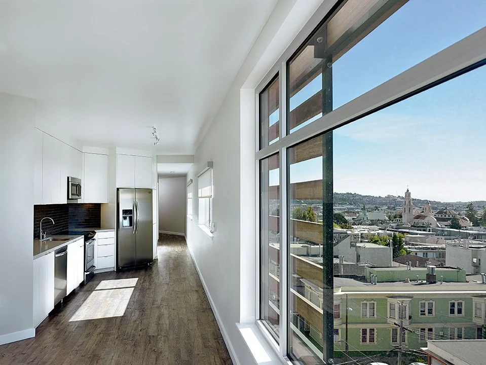 Empty modern kitchen with white cabinets, stainless steel appliances, and large window overlooking a cityscape with buildings and a church tower.