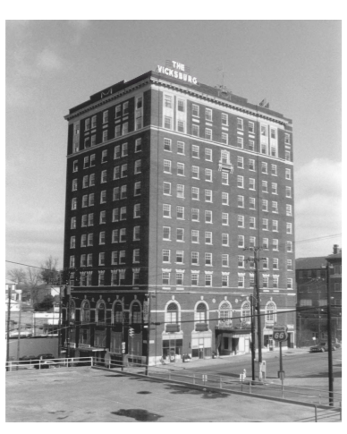 A black and white photo of a tall brick hotel called The Vicksburg, with multiple floors and a street view including streetcar tracks, signs, and utility poles.