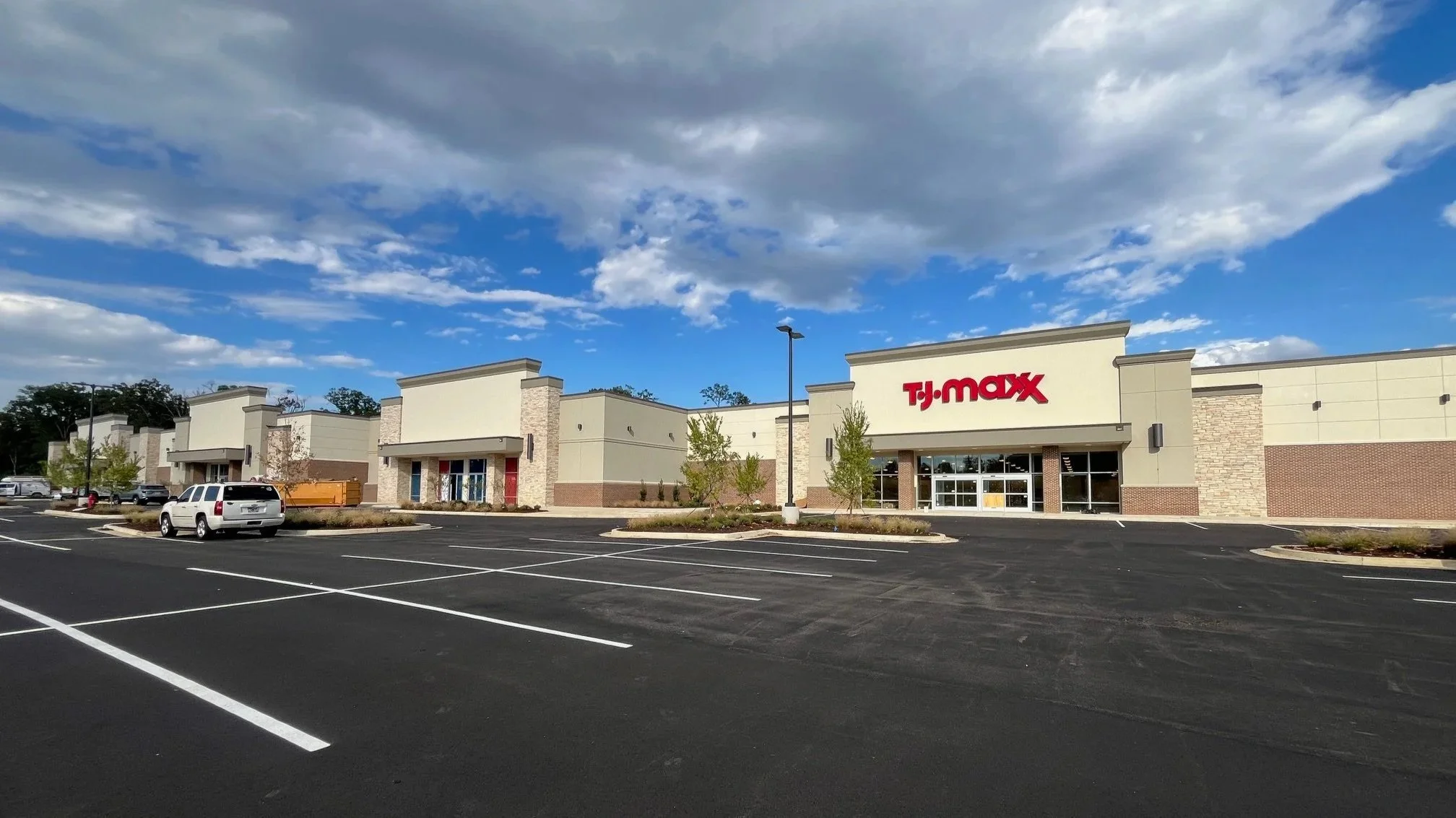 An empty parking lot in front of a TJ Maxx retail store under a partly cloudy sky.
