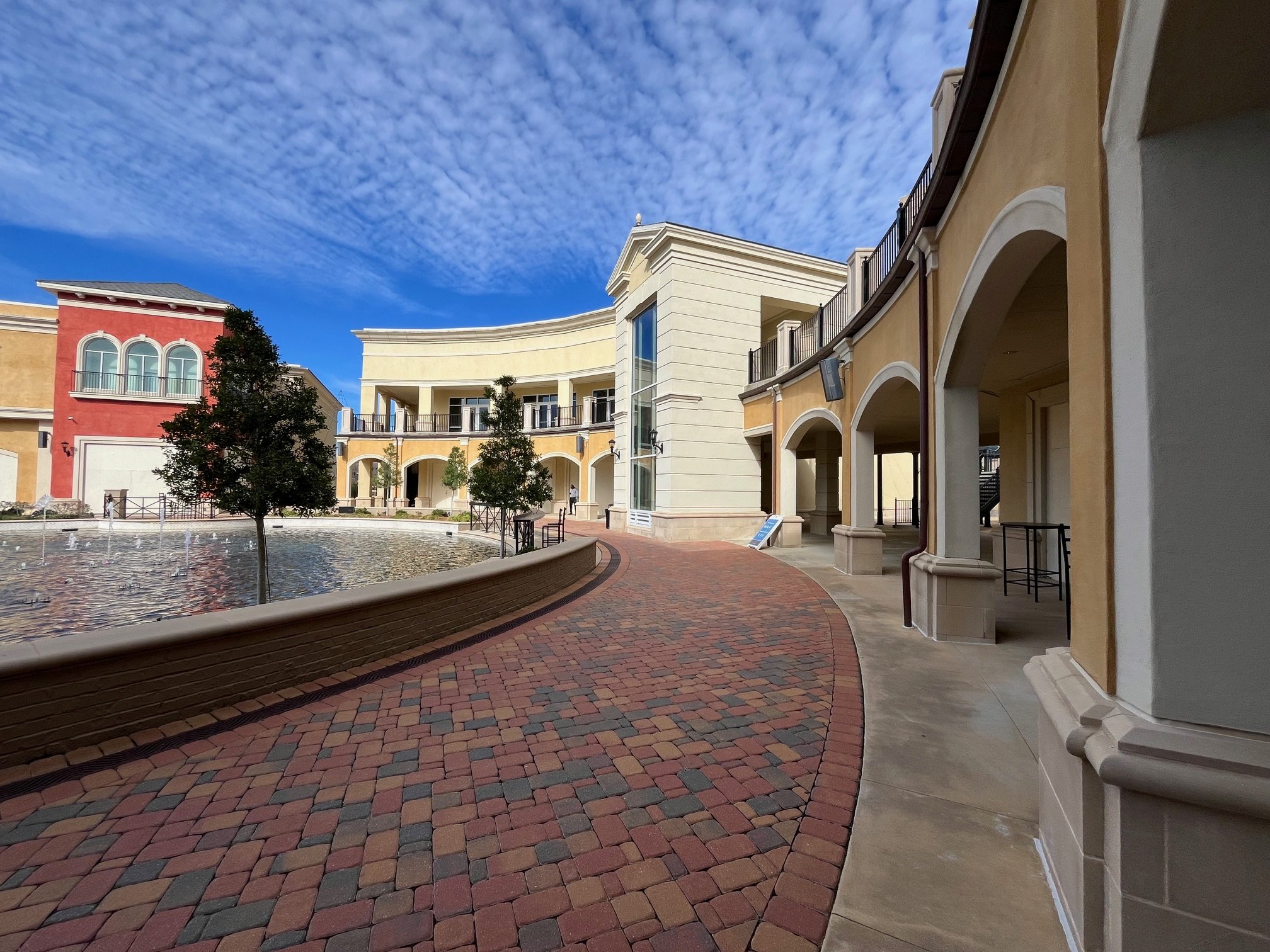 Renaissance Lofts at Colony Park, Ridgeland, MS.  A colorful outdoor courtyard with a fountain, trees, and European-style buildings under a partly cloudy sky.