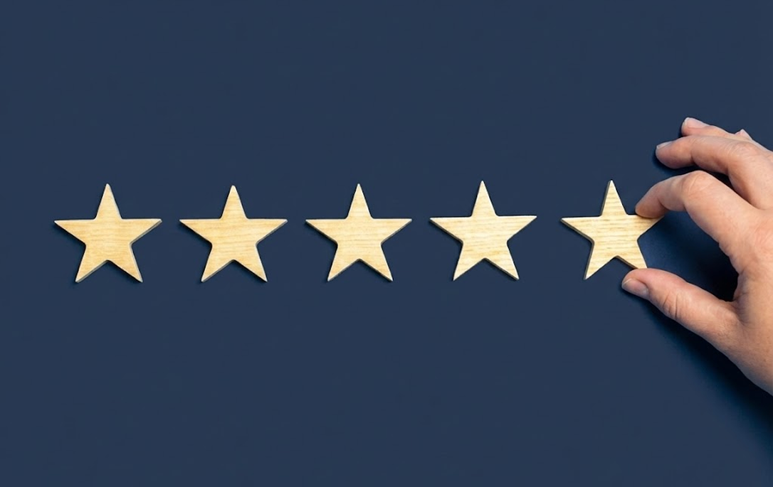 Hand placing a wooden star on a row of five wooden stars against a dark blue background.
