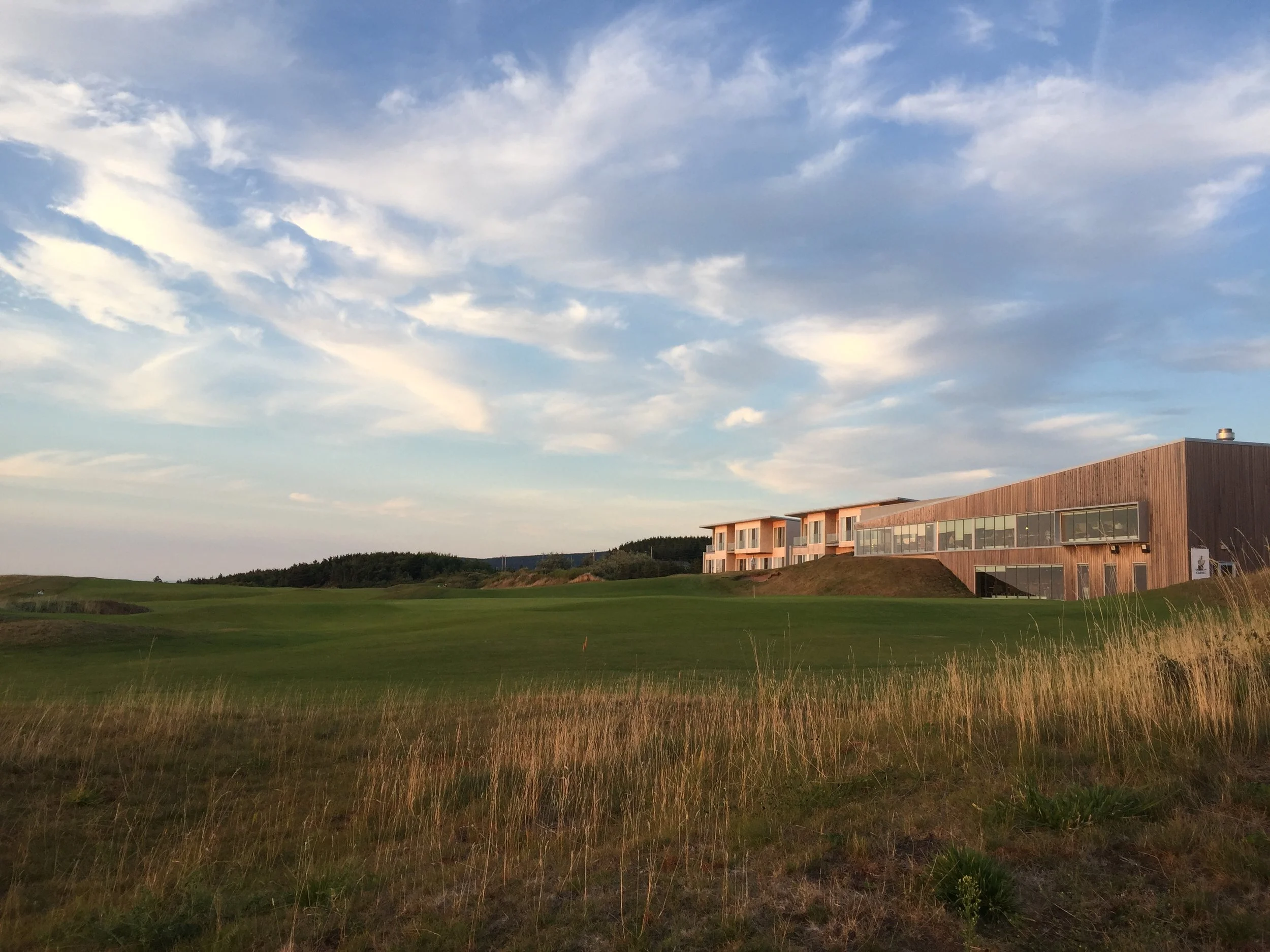 Modern building with large windows on a grassy landscape under a partly cloudy sky.