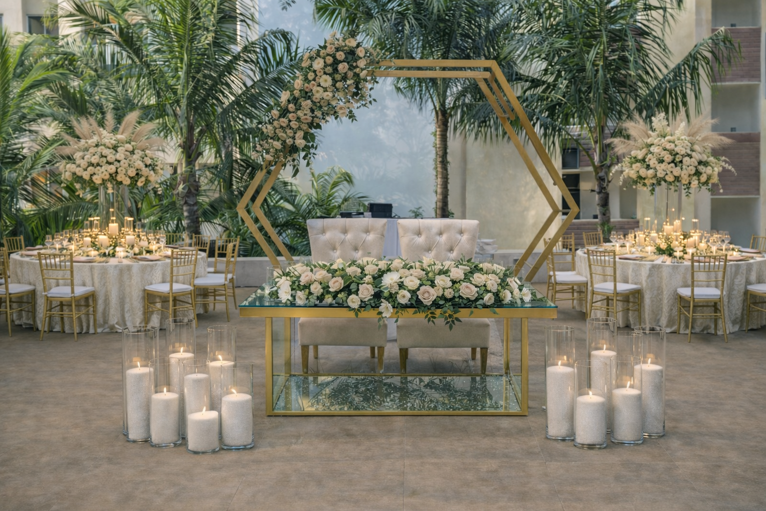 Elegant wedding ceremony setup with a floral arch, white sofas, and tables decorated with candles and flowers in a tropical indoor setting.