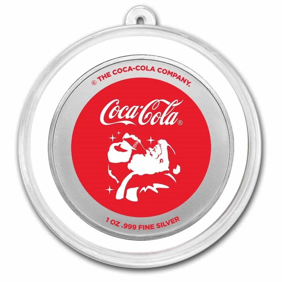 A round silver container with a red and white label featuring a Santa Claus figure pouring a Coca-Cola, with the Coca-Cola logo above. Text around the label reads "The Coca-Cola Company" and "1 Oz. 999 Fine Silver."