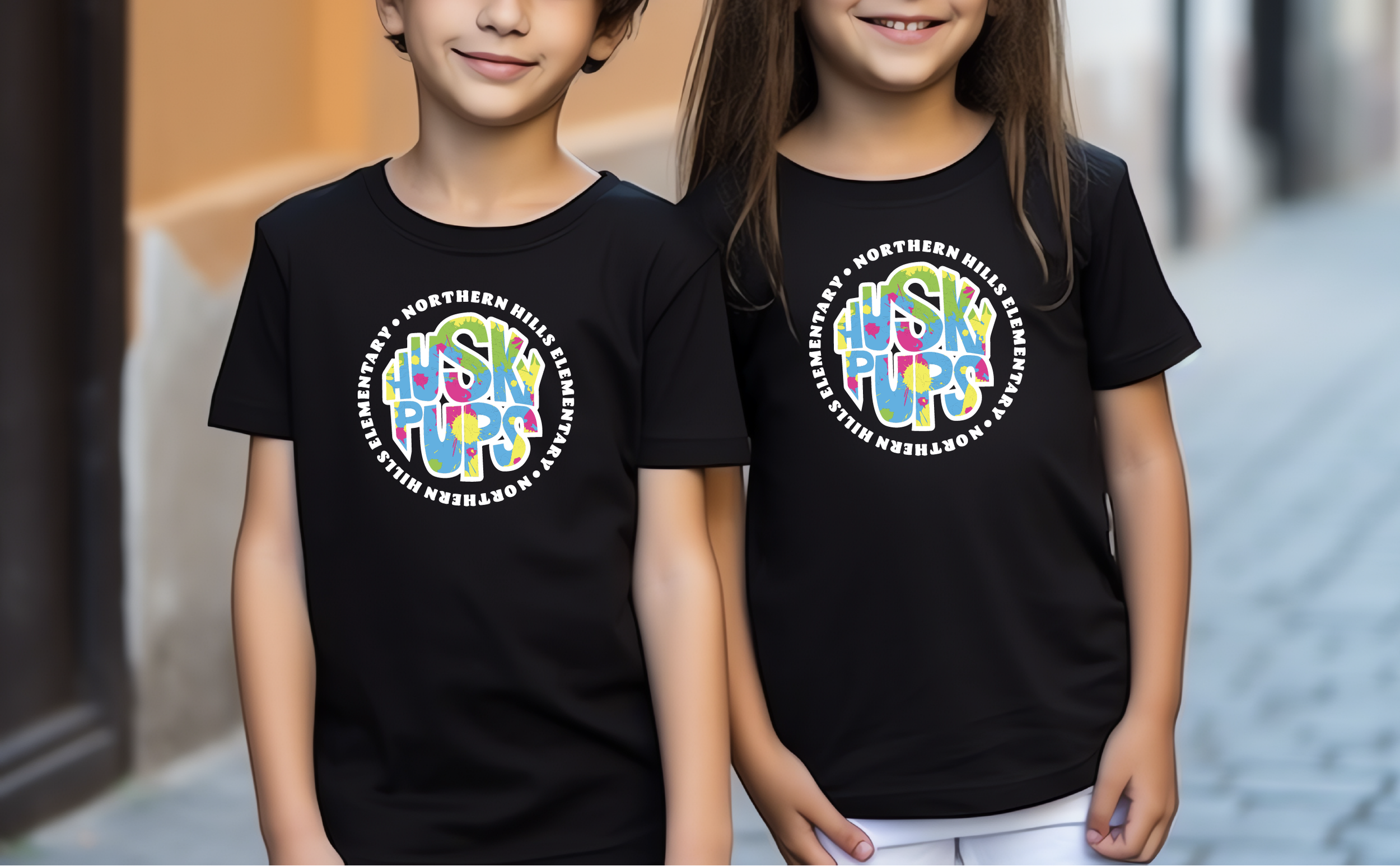 Two children wearing black T-shirts with colorful logo and text, standing outdoors, smiling.