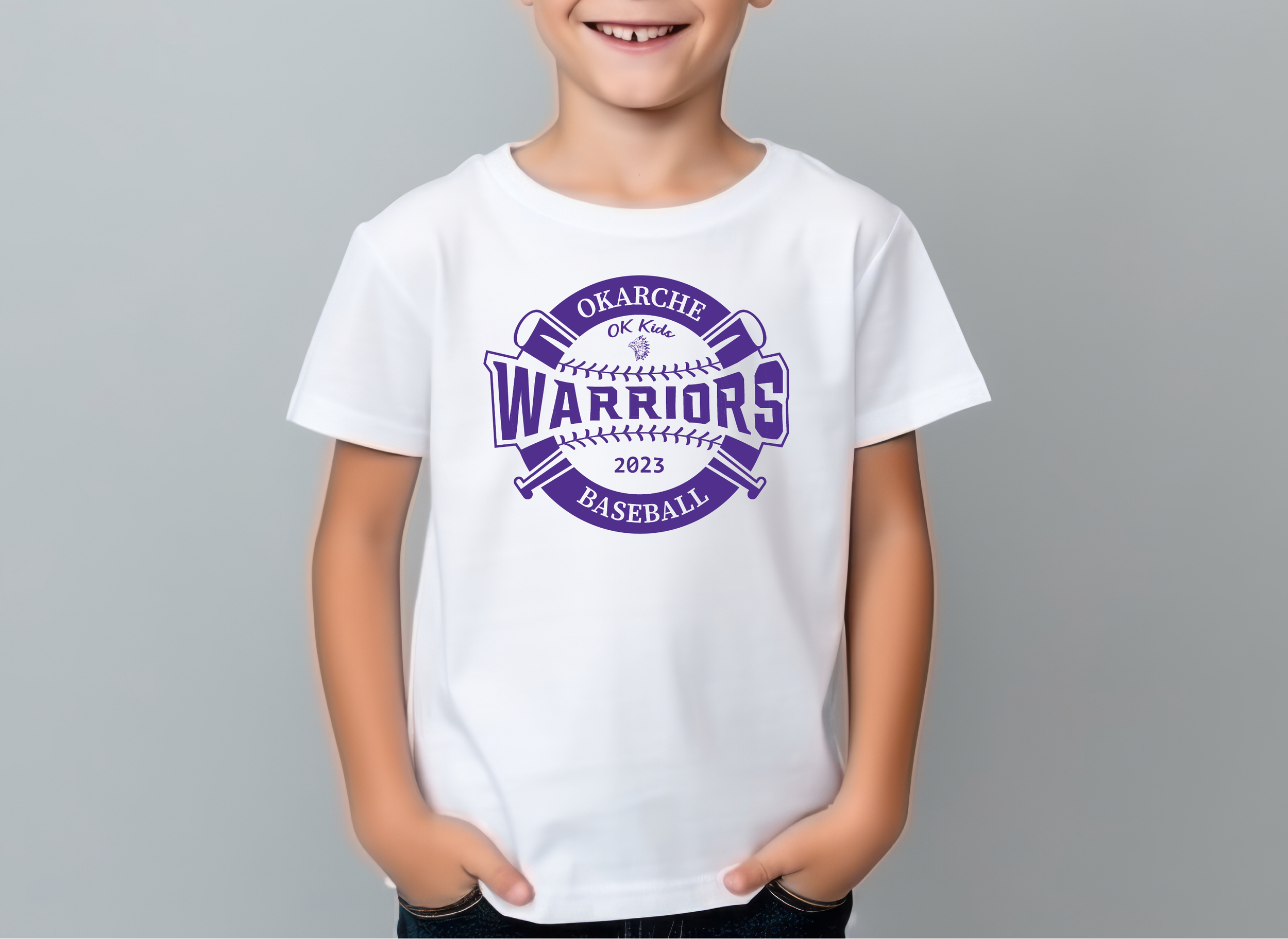 Child wearing a white T-shirt with purple logo reading "O KARCHE OK Kids WARRIORS BASEBALL 2023" with two crossed baseball bats.