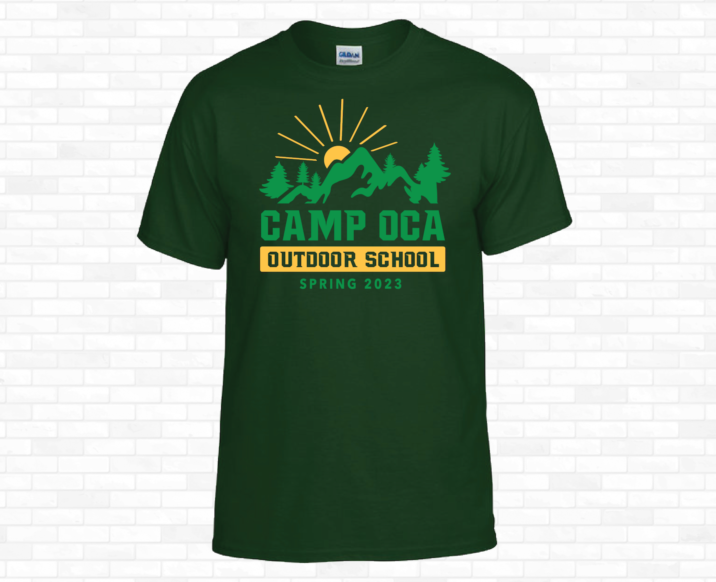 Green T-shirt with a design featuring mountains, pine trees, a rising sun, and text that reads "Camp Oca Outdoor School Spring 2023."