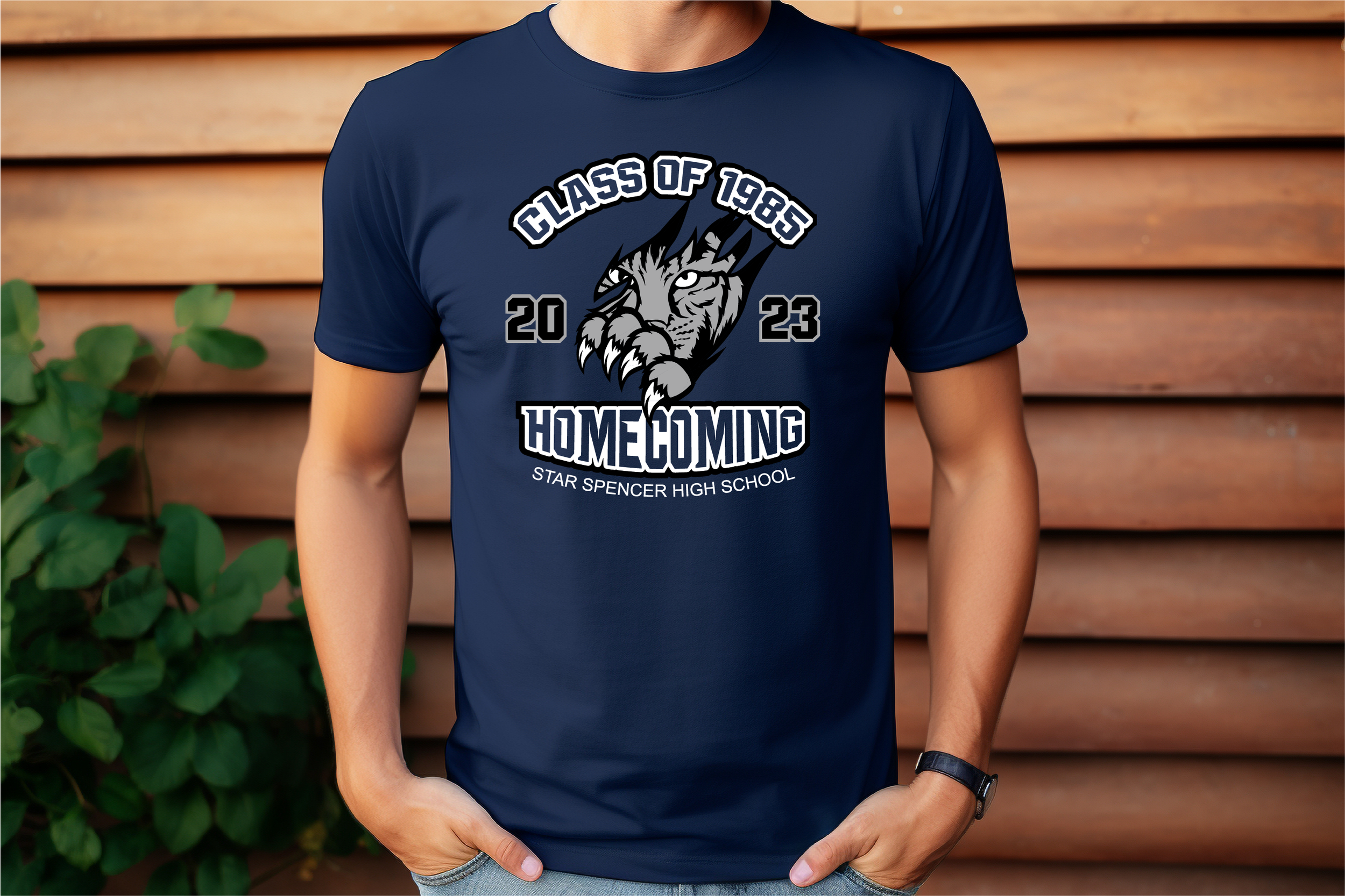 A person wearing a navy blue T-shirt with a graphic design for Star Spencer High School's 2023 homecoming. The design features a fierce tiger's face in black, gray, and white, with the text "Class of 1985" above, "Homecoming" below, and the school na