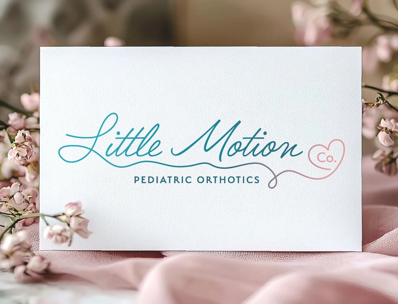 A light-colored sign with the text 'Little Motion Co. Pediatric Orthotics' surrounded by pink flowers and pink fabric.
