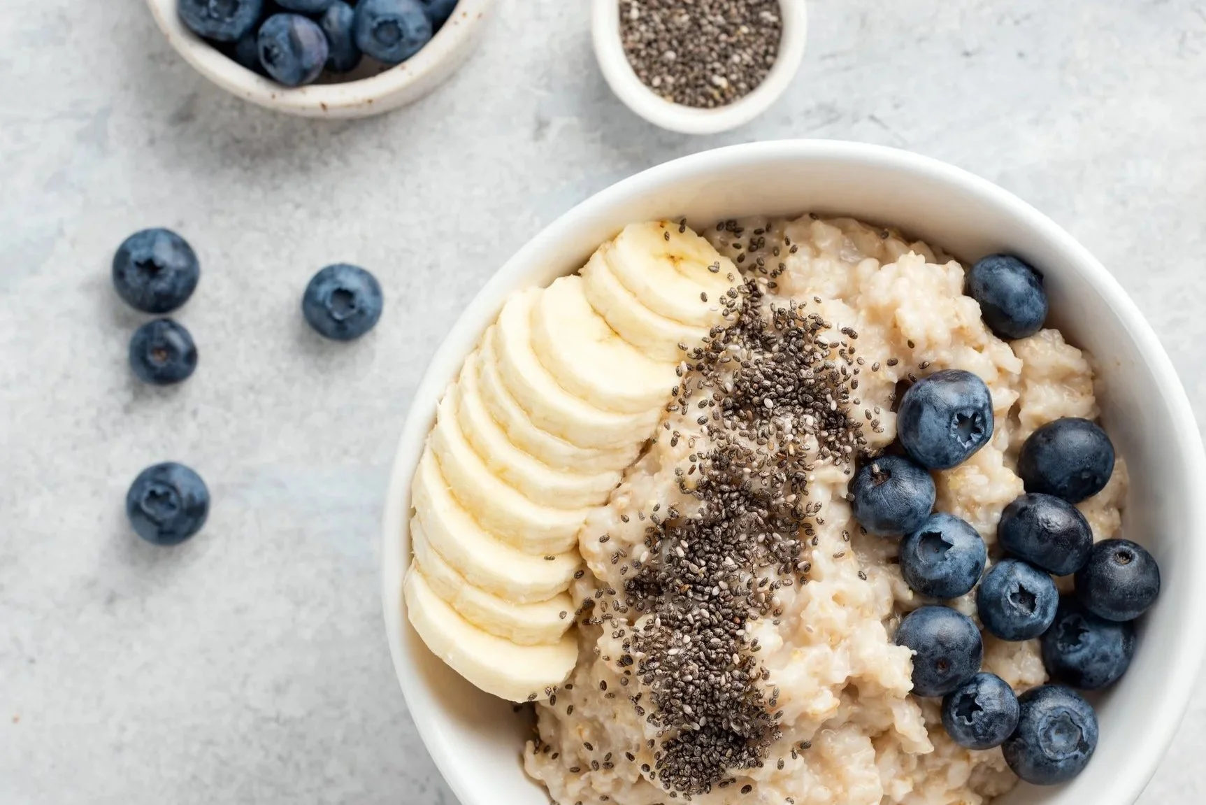 A bowl of oatmeal topped with sliced banana, blueberries, chia seeds, and flax seeds.