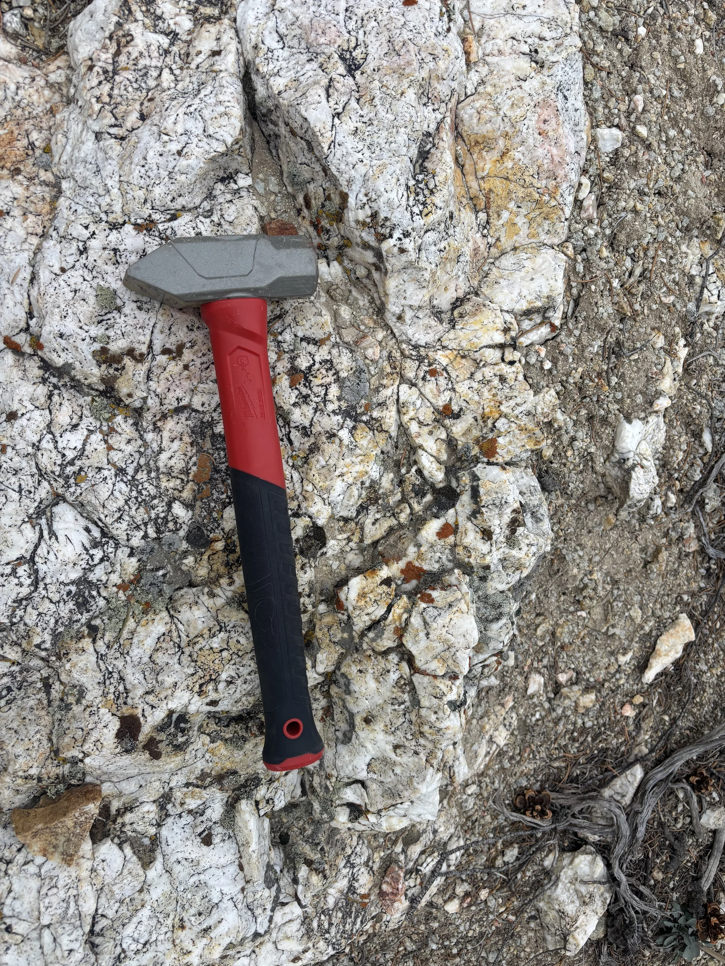 A hammer with a red handle and gray head resting on a rocky surface.