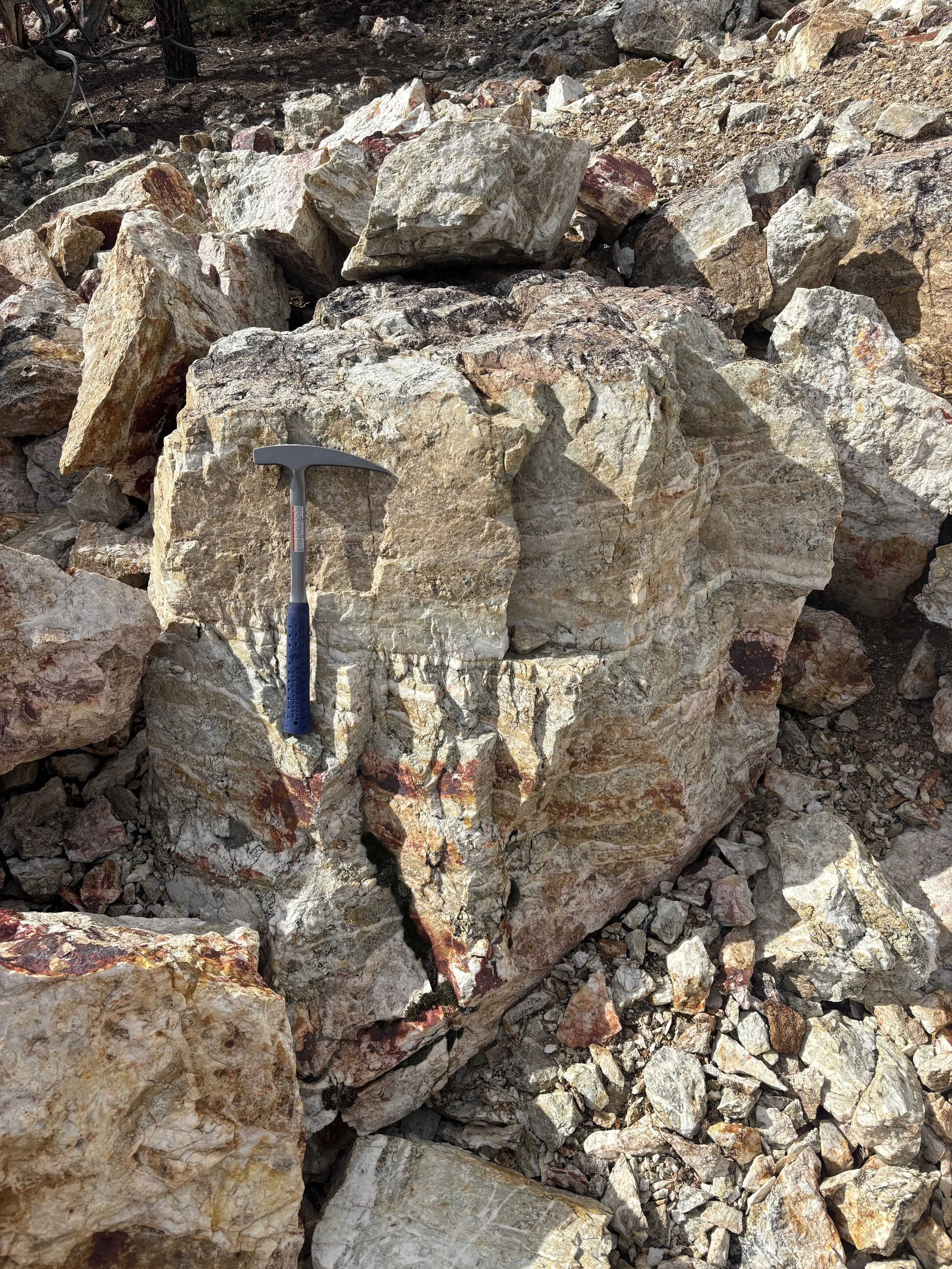 Collection of large, rugged rocks and stones with an ice axe placed among them, suggesting climbing or geological activity at a rocky outdoor location.