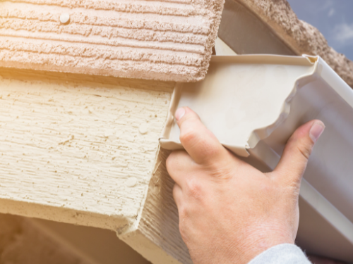 Close-up of a person's hand applying caulk to the corner of a wall and ceiling.