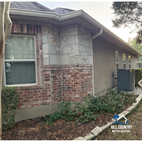 Close-up of a residential house corner showing a brick and stone exterior, with a window with blinds, and an air conditioning unit outside.