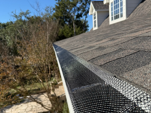 Close-up of a house's gutter with a leaf guard screen installed, with the roof and sky in the background.