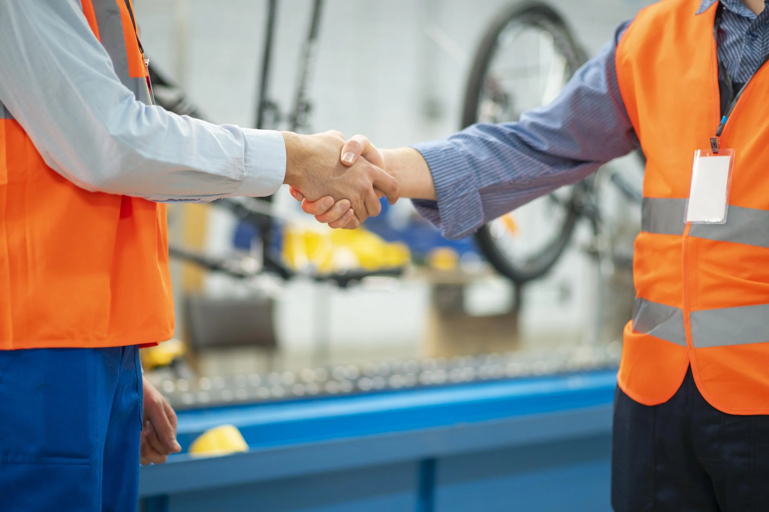 Two workers in safety vests shaking hands in a bicycle workshop.